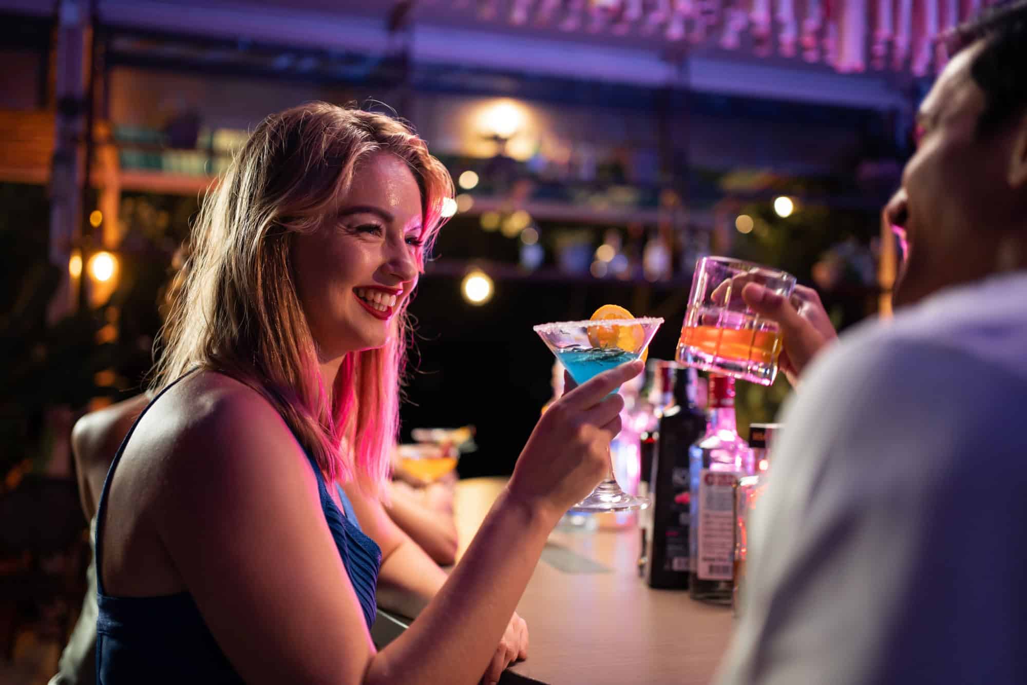 Beautiful young couple having fun, drinking alcohol cocktail in a bar. Attractive friend man and woman feeling happy and relax having a party, drink a glass of beer to celebrating event at night club.