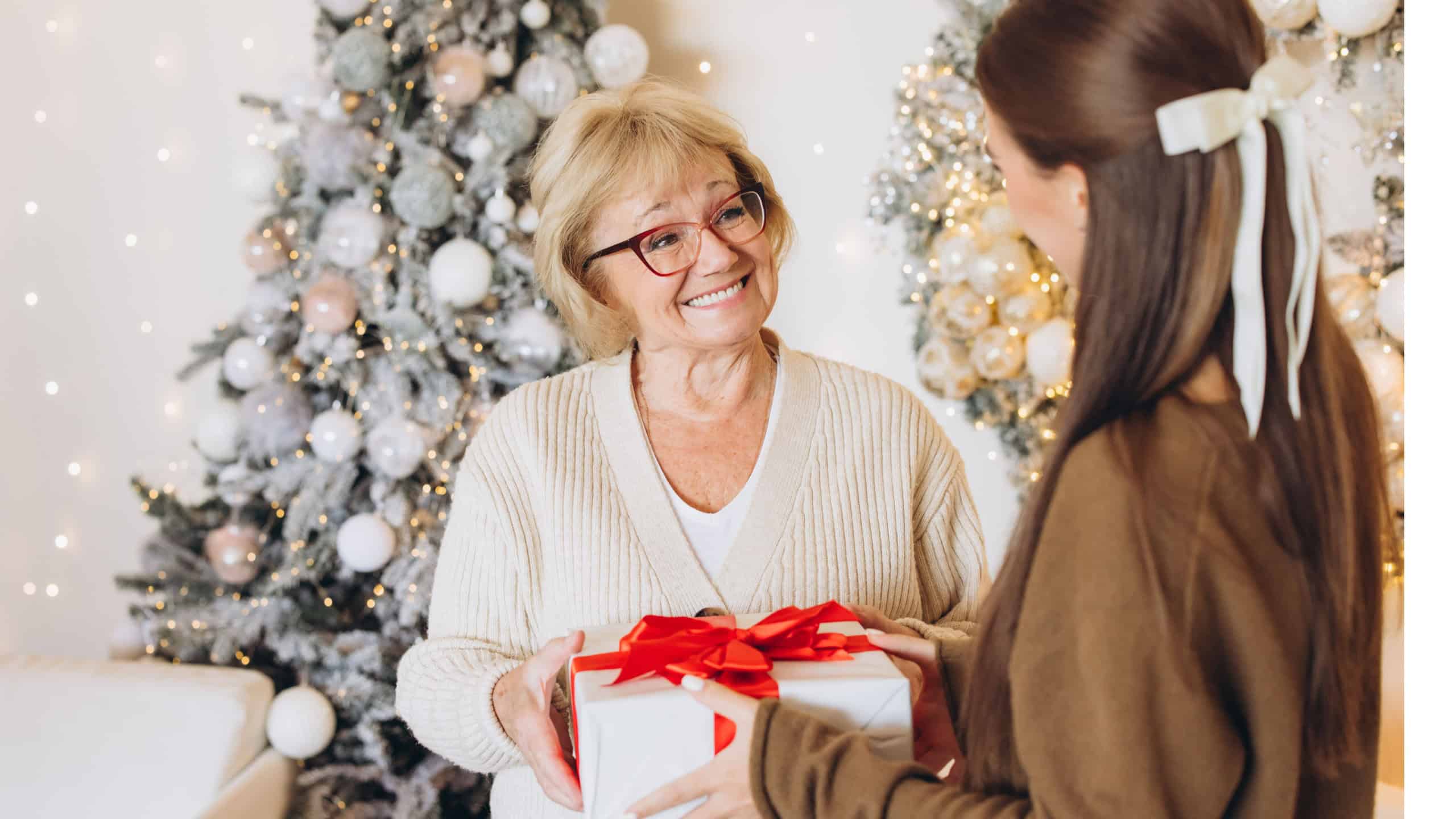 A happy grandmother receives a wrapped gift from her granddaughter in beautifully decorated living room with a Christmas tree. The festive atmosphere captures the warmth and joy of the holiday season.