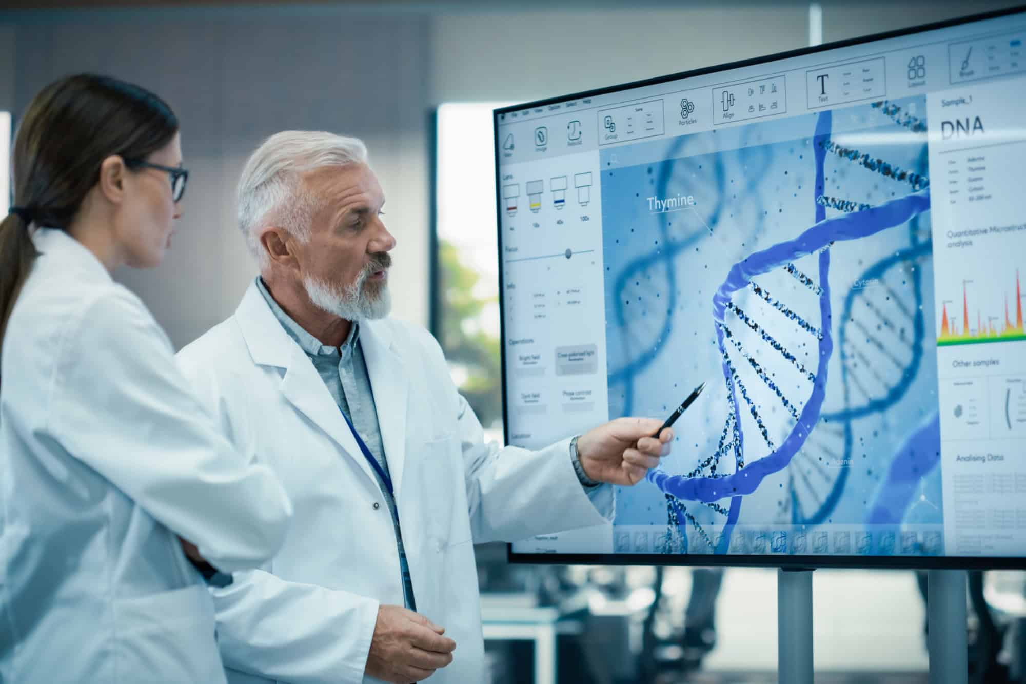 Middle Aged Head of Laboratory Having a Meeting with a Female Chief Technologist in a Modern Biochemistry Lab. Colleagues Looking at a Screen and Having a Conversation About DNA
