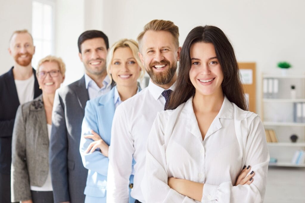 Smiling supportive diverse businesspeople team standing, confident excited male, female employees happy with job promotion or hr success, colleagues enjoy work achievement, welcoming new member