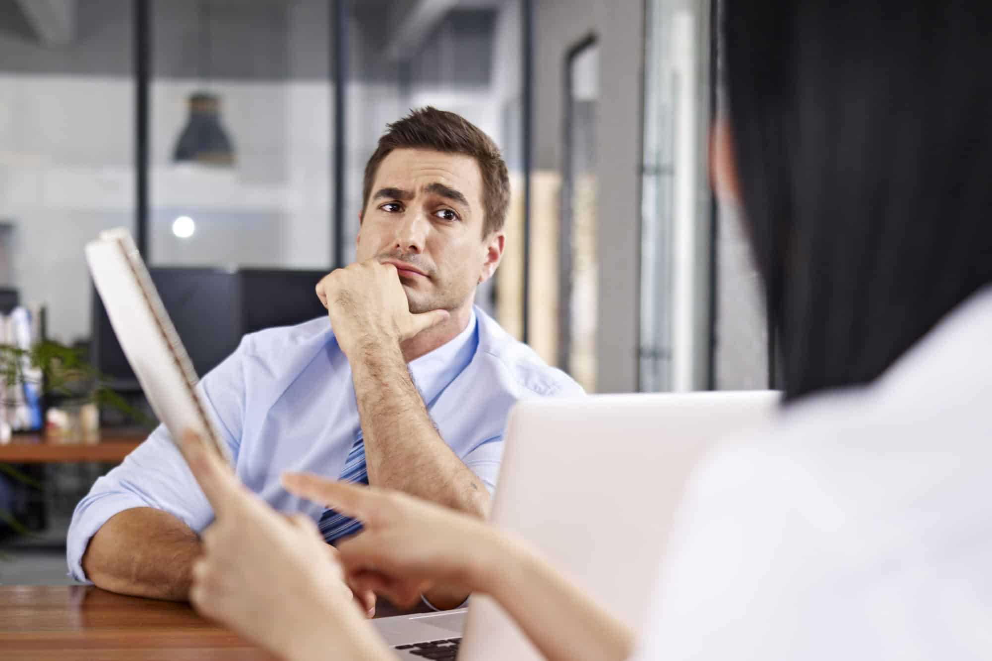 a caucasian male interviewer looking skeptical while listening to an asian female interviewee.