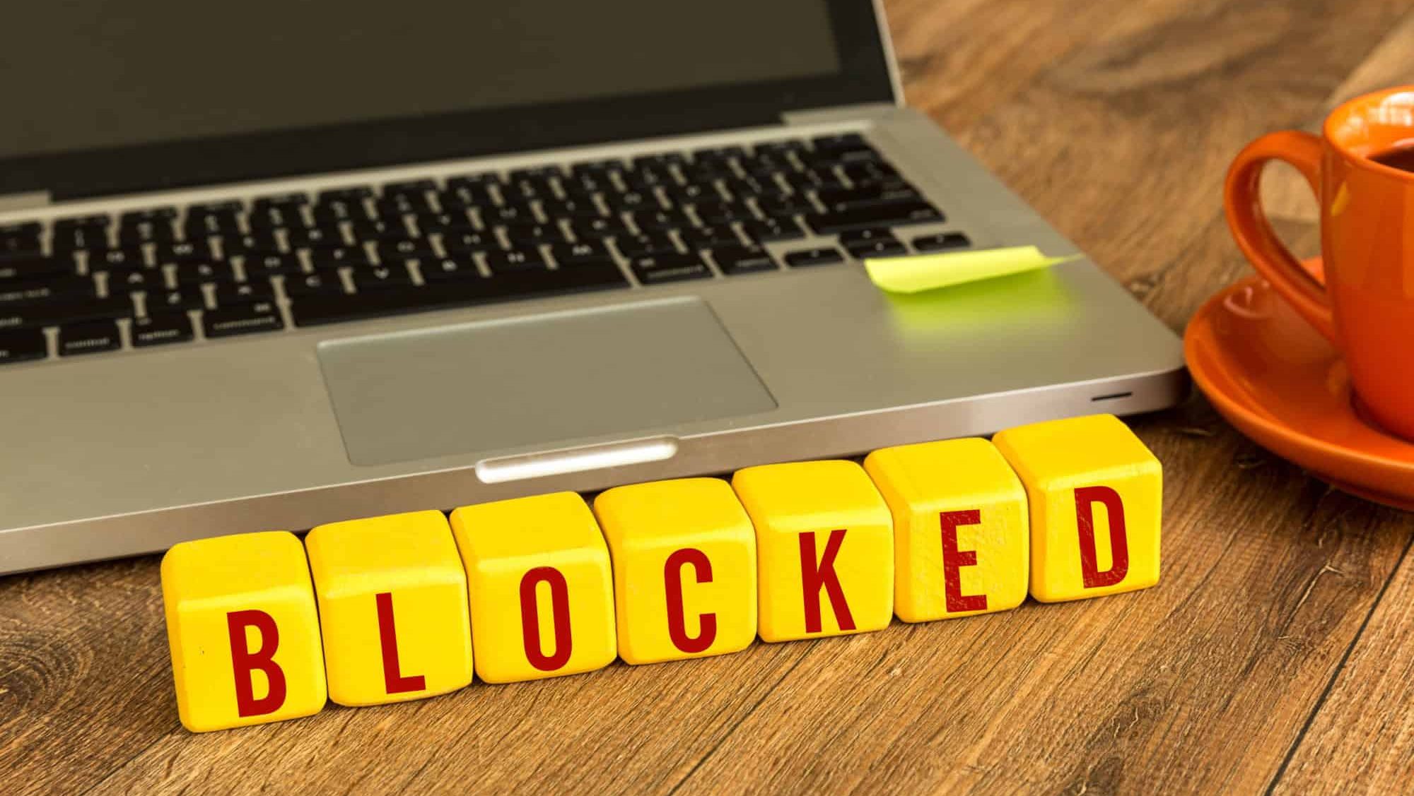 Blocked written on a wooden cube in front of a laptop