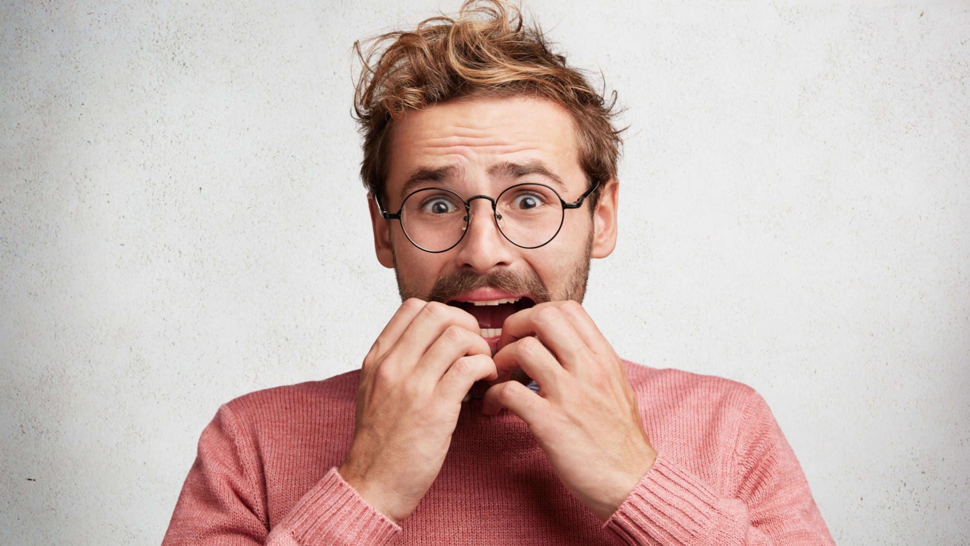 Embarrased nervous male looks scared and worried, bites nails, has sorrorful and frightened expression, expresses negative emotions. Amazed scared young clever man worries before job interview