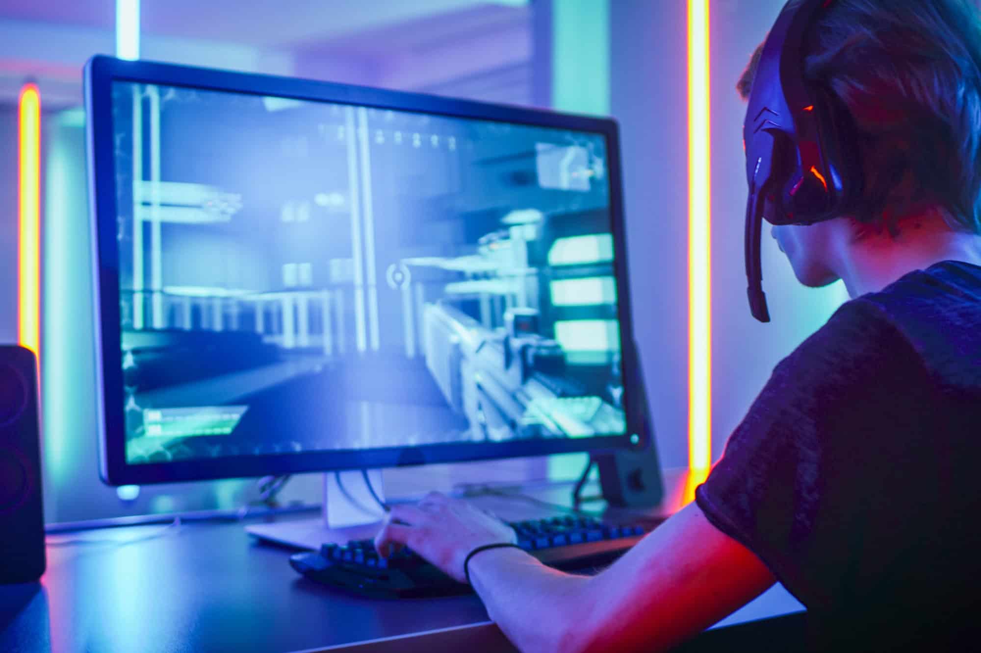 Shot of the Professional Gamer Playing in First-Person Shooter Online Video Game on His Personal Computer. Room Lit by Neon Lights in Retro Arcade Style. Online Cyber e-Sport Internet Championship.