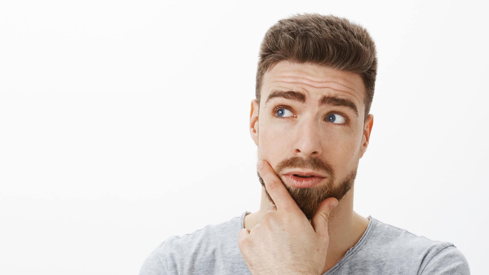Curious and questioned handsome businessman trying solve problem thinking standing in thoughtful pose rubbing beard looking at upper left corner making decision against gray background