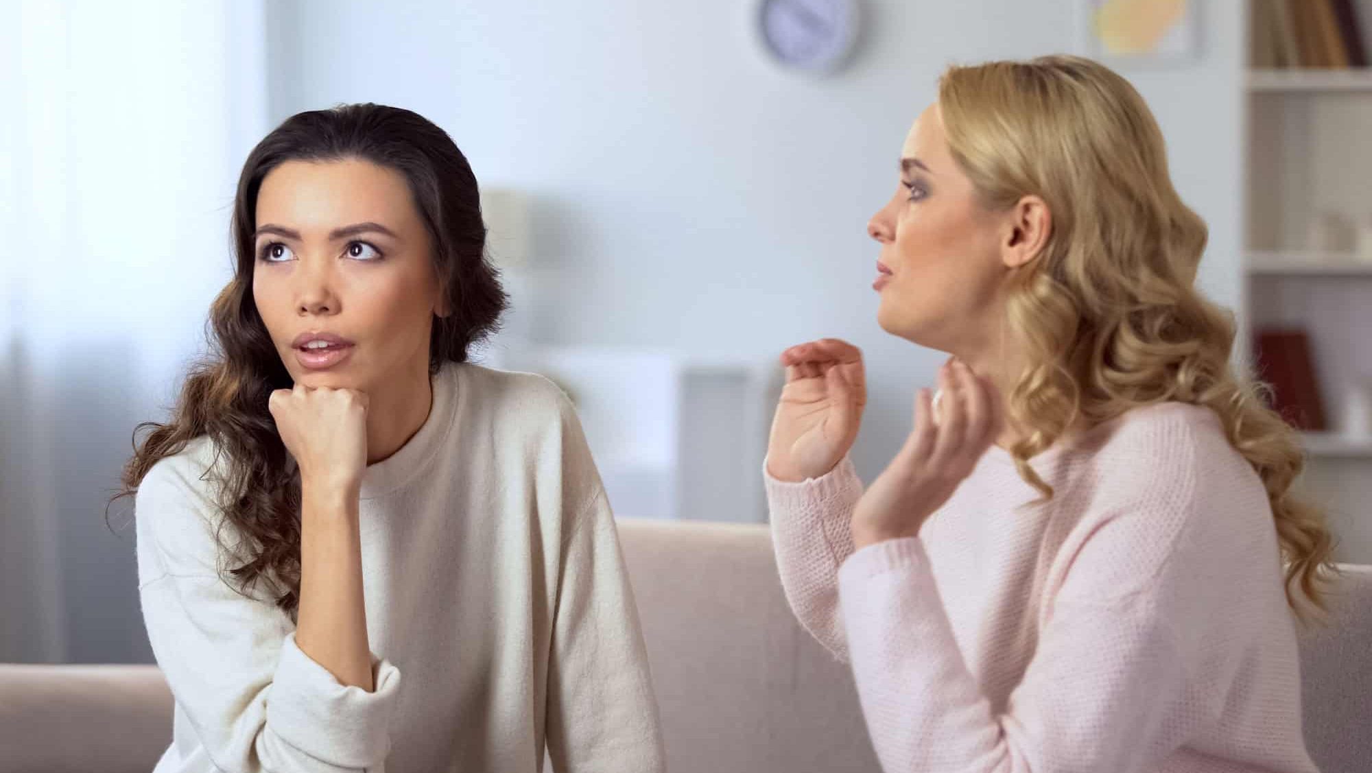 Young lady getting bored about conversation with her friend, fake relationship
