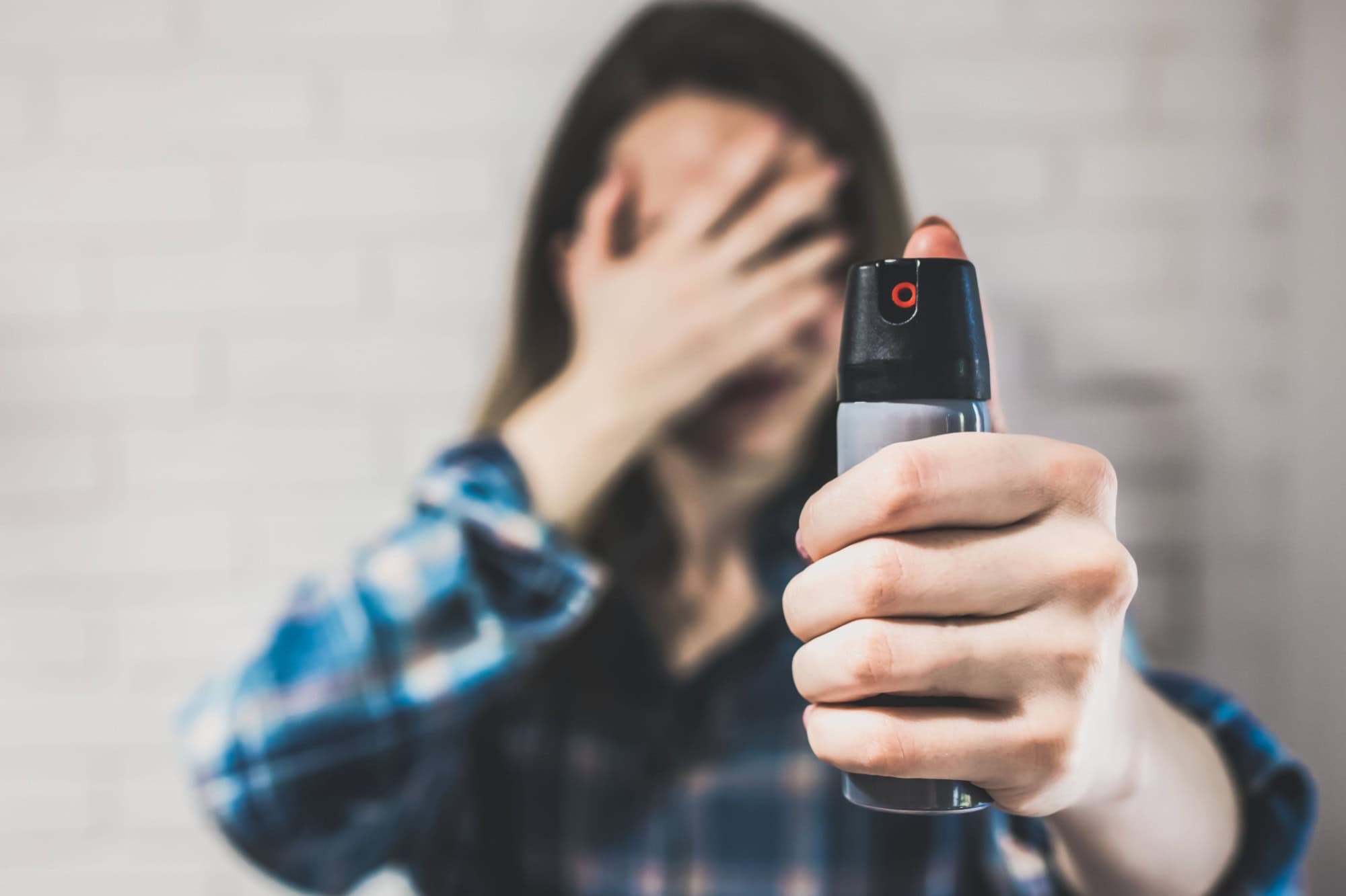Married woman is holding pepper spray canister for personal protection. Girl covers her face with hands. White background behind. Self-defense photo. Copy space place.