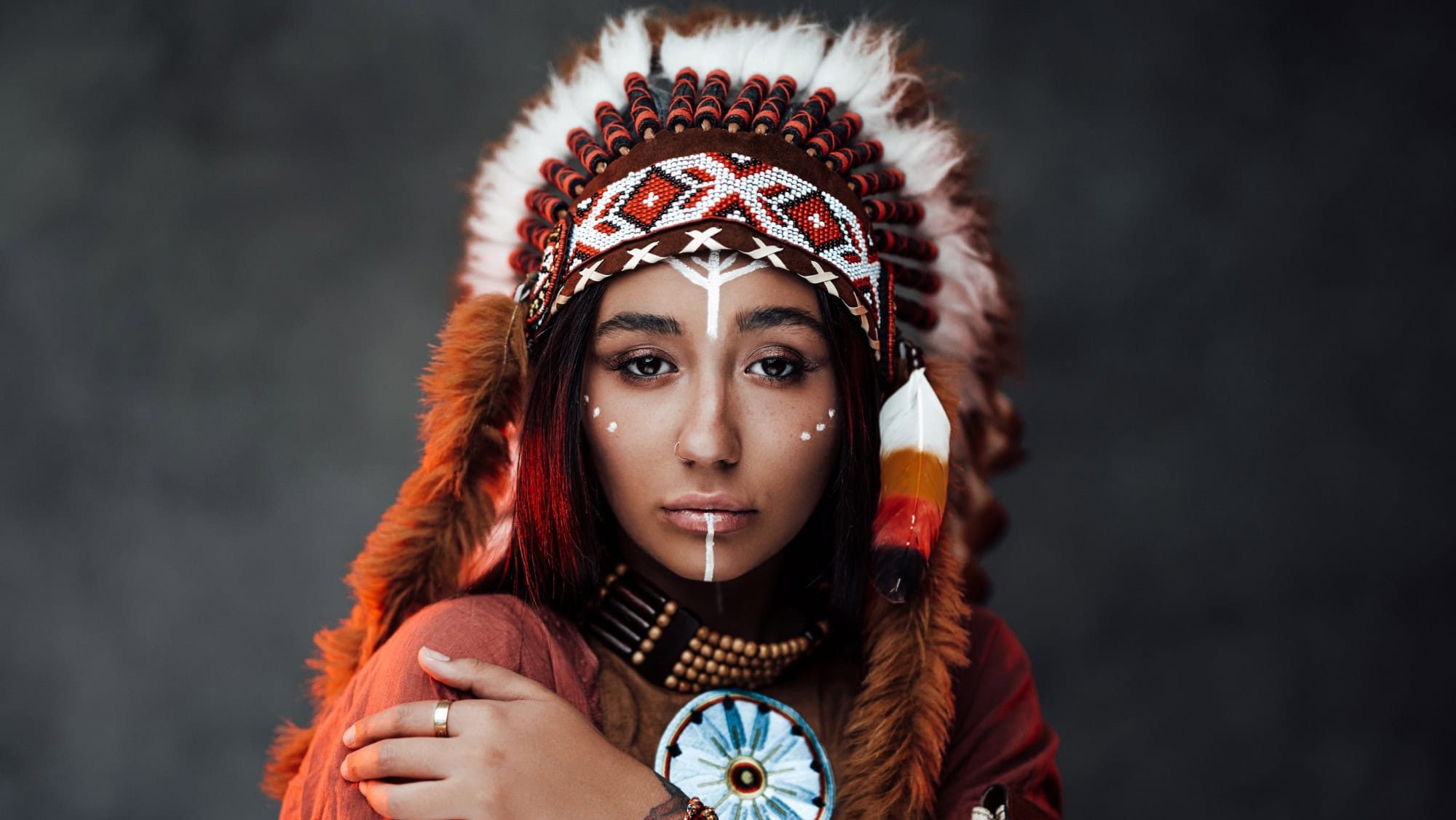 Studio portrait of a beautiful Native American girl with tattoo on hand in colorful traditional ethnic costume on a dark background