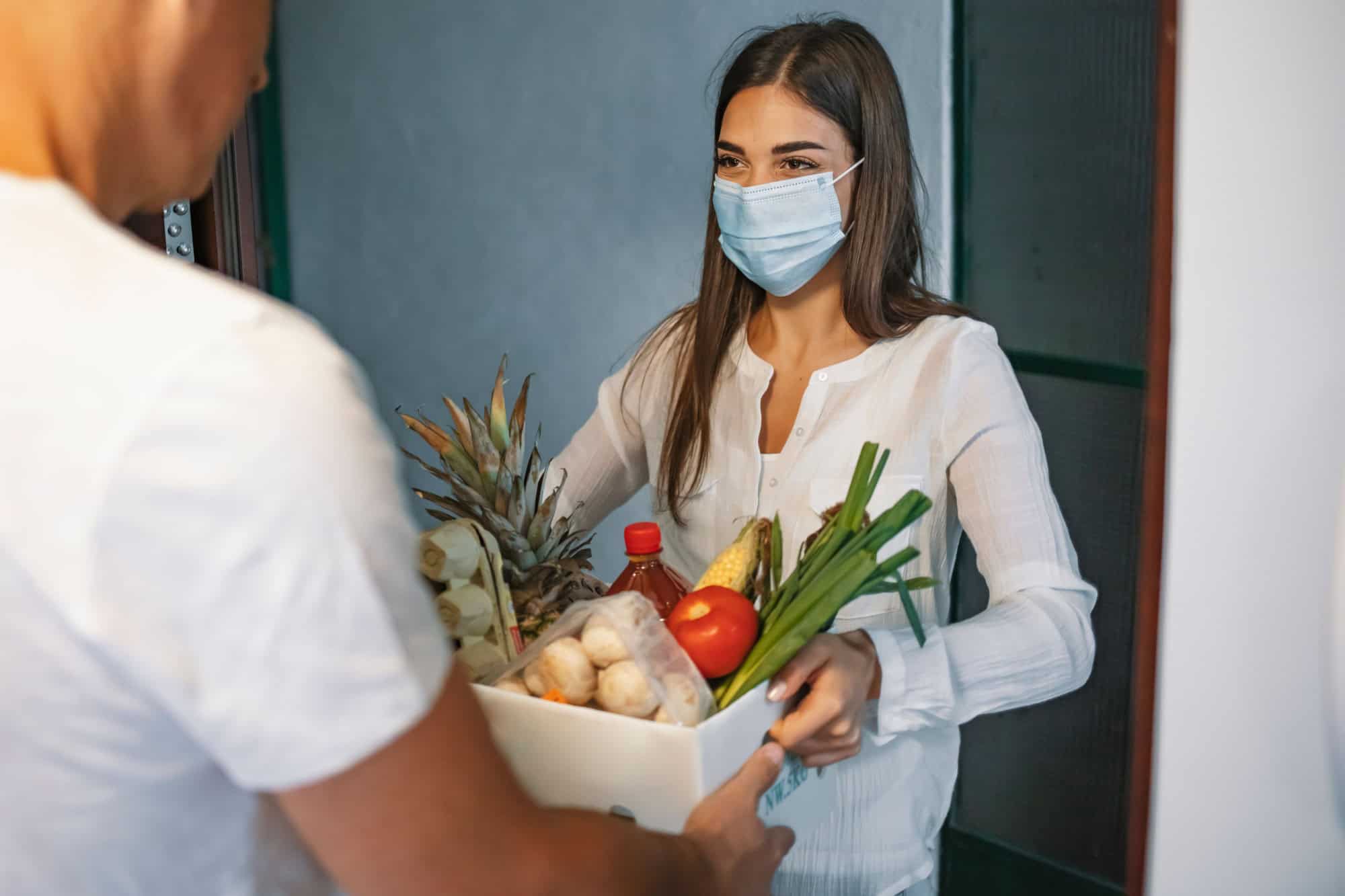 Volunteer Bringing food to old and disability people in quarantine. Food delivery during covid-19. Woman at open door delivering fresh food in box during covid-19 coronavirus crisis curfew quarantine