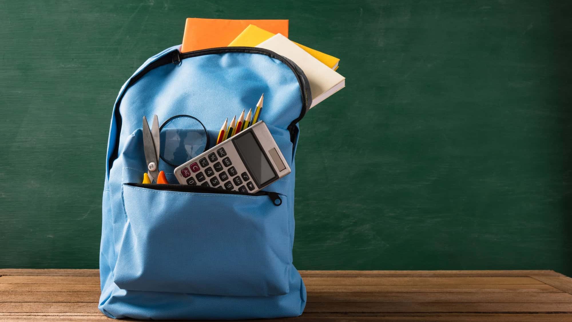 Front of stylish school bag backpack and stationery accessory on a table desk at the green chalkboard, Back to school education concept