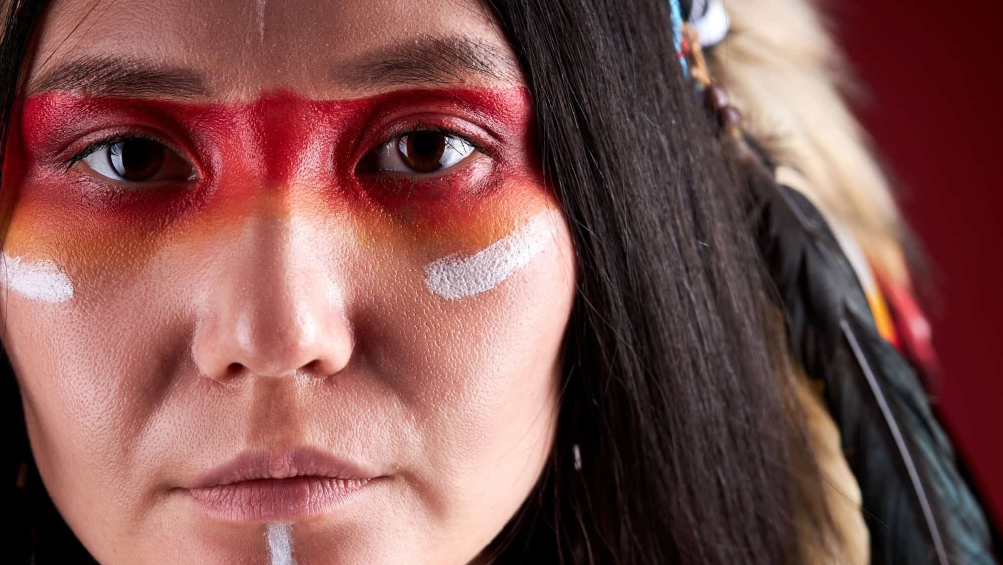 close-up portrait in native american style, beautiful woman in Indian hat and drawings on face, trendy color photo. accessories Bohemians and Boho