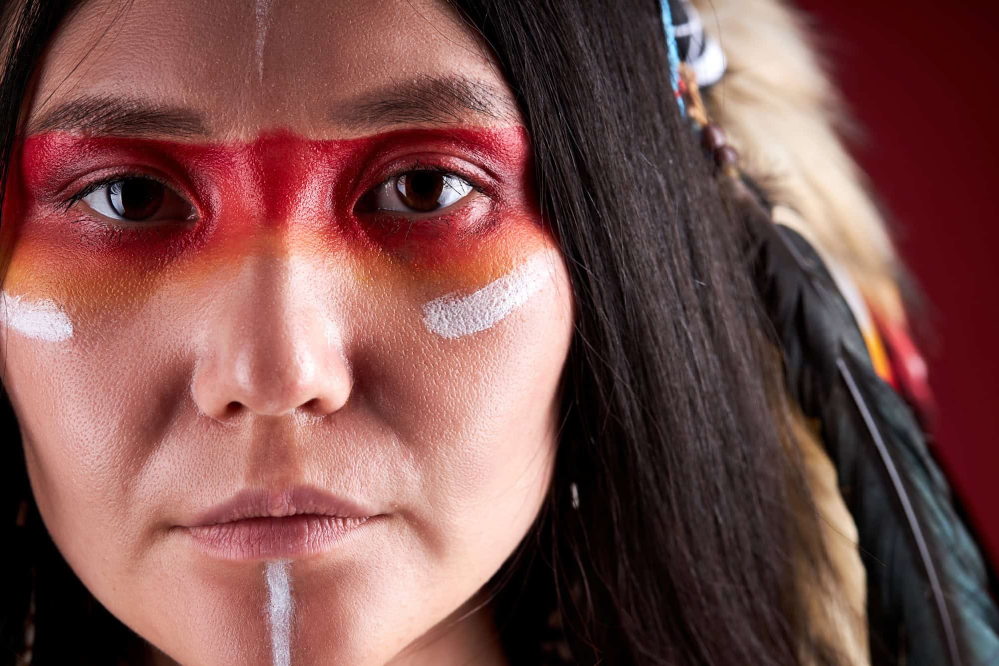 close-up portrait in native american style, beautiful woman in Indian hat and drawings on face, trendy color photo. accessories Bohemians and Boho