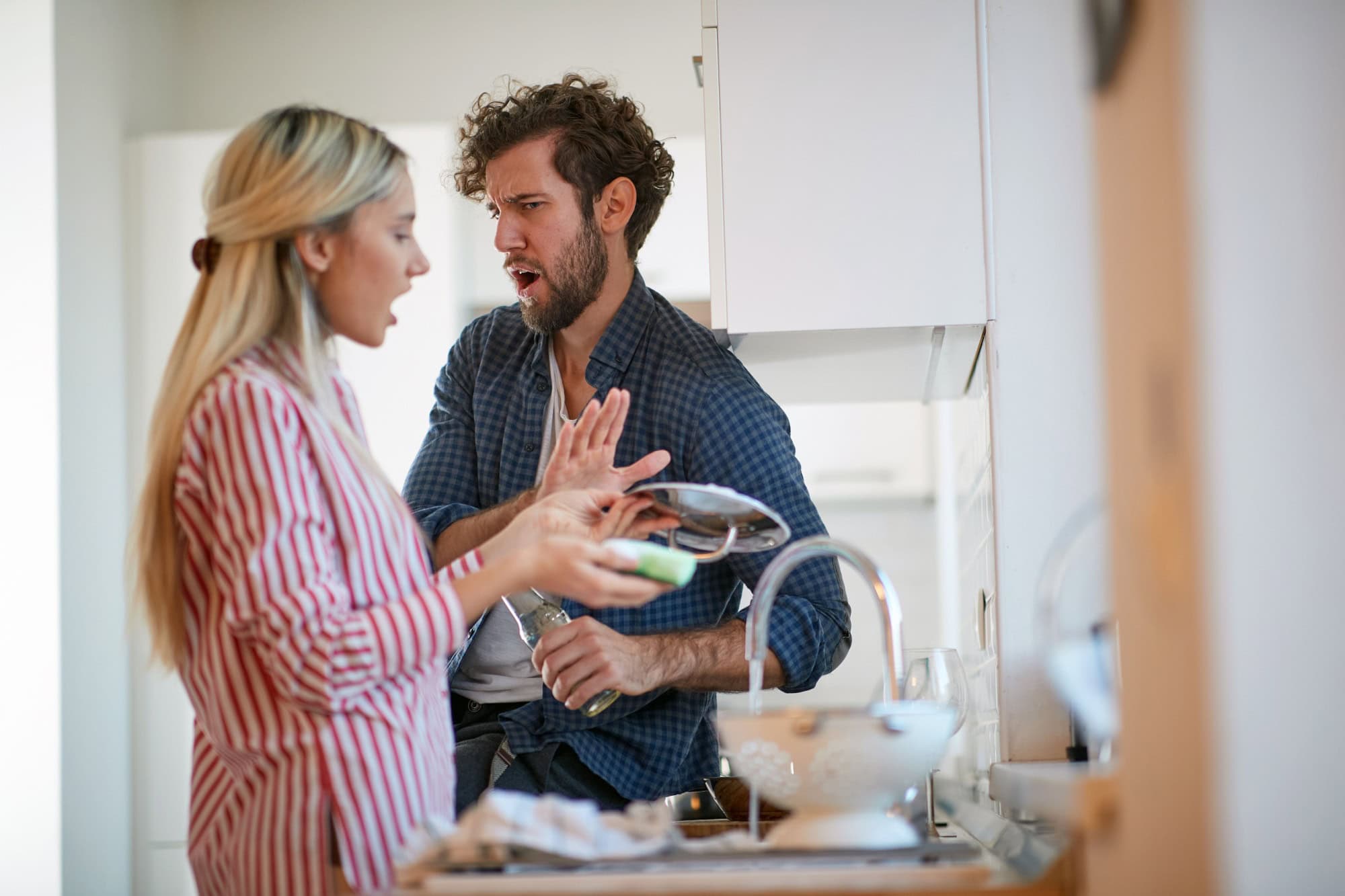 A young couple arguing about housework in a tense atmosphere at the kitchen. Kitchen, housework, home, relationship
