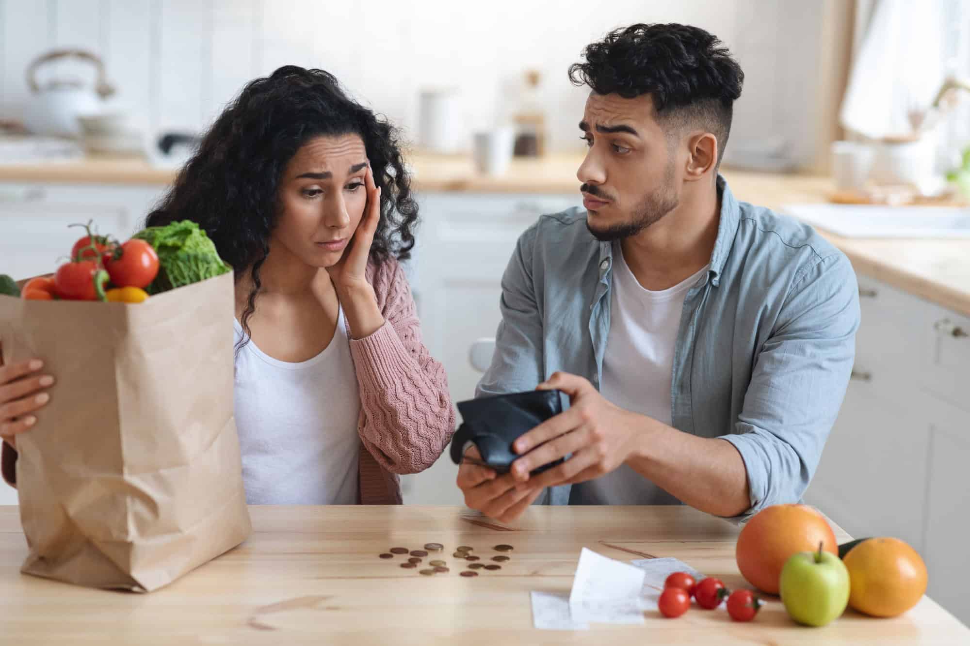 Coronacriris Concept. Depressed Arab Couple In Kitchen Counting Remaining Money After Food Shopping, Upset Middle Eastern Spouses Looking At Empty Wallet, Shocked By Big Prices For Grocery, Closeup