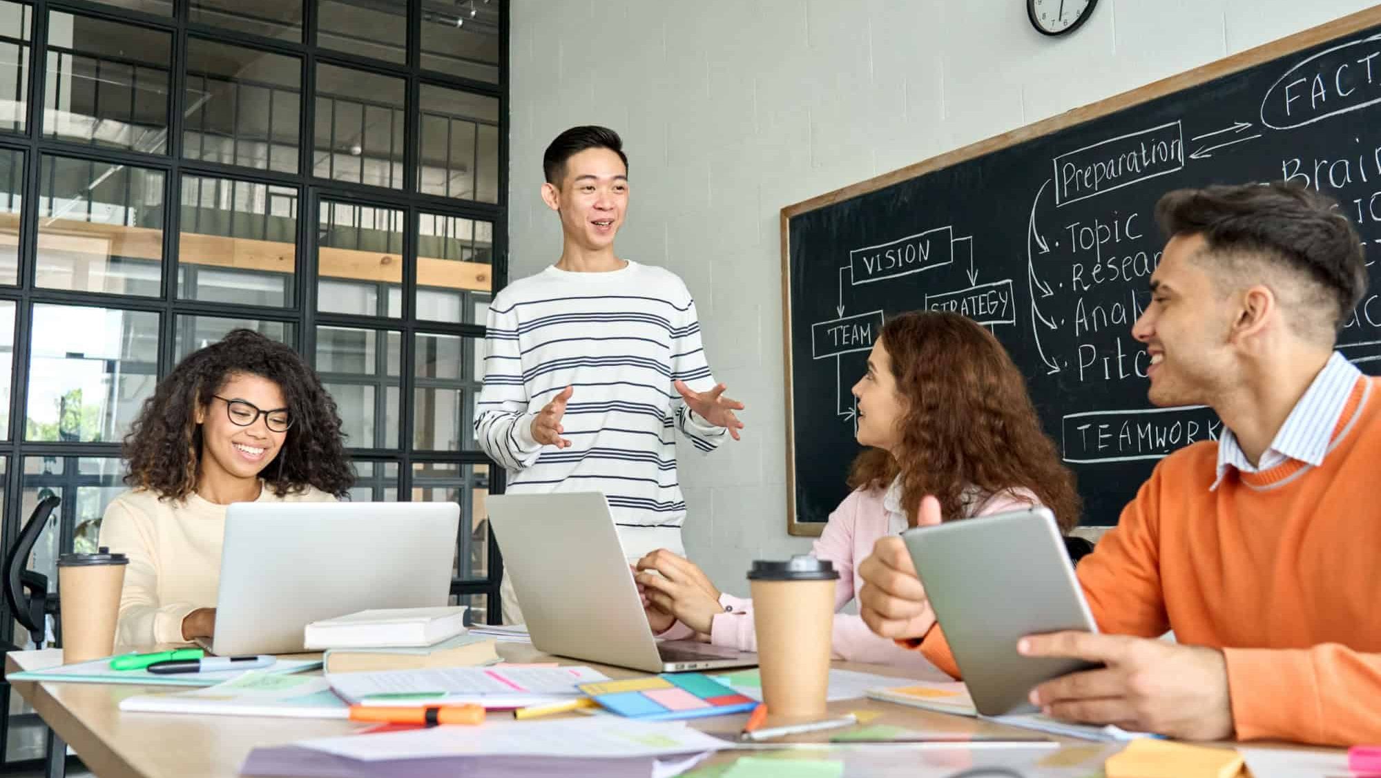 Four diverse multiracial young professional business startup gen z team students group working on project listen to Asian leader in contemporary office classroom with gadgets. Diversity concept.