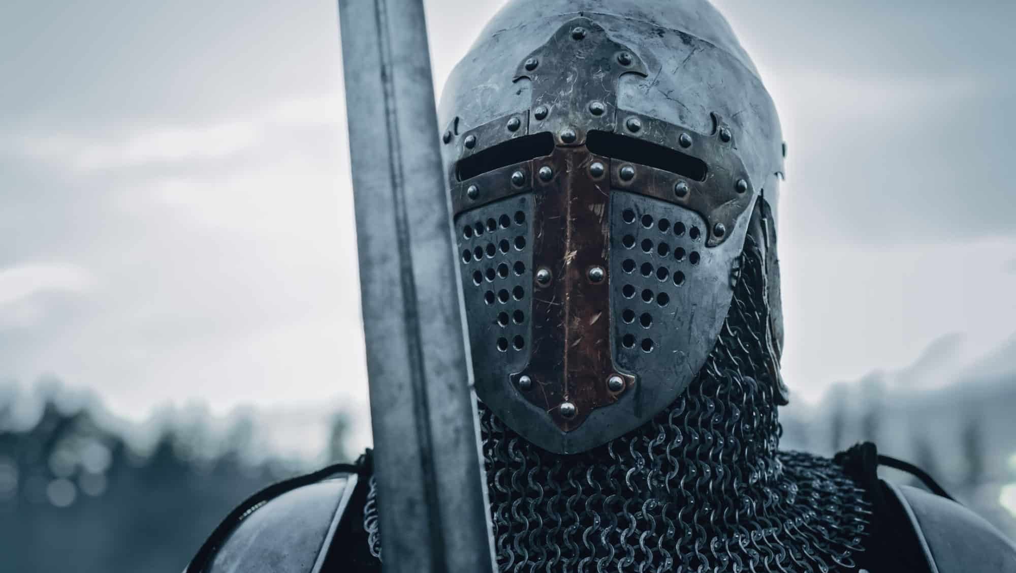 Medieval Knight Wearing Armour and Helmet, Draws Sword from Shearh, Ready to Fight, Kill His Enemy in Battle. Warrior Soldier on Battlefield. War, Invasion, Crusade. Cinematic Historic Reenactment