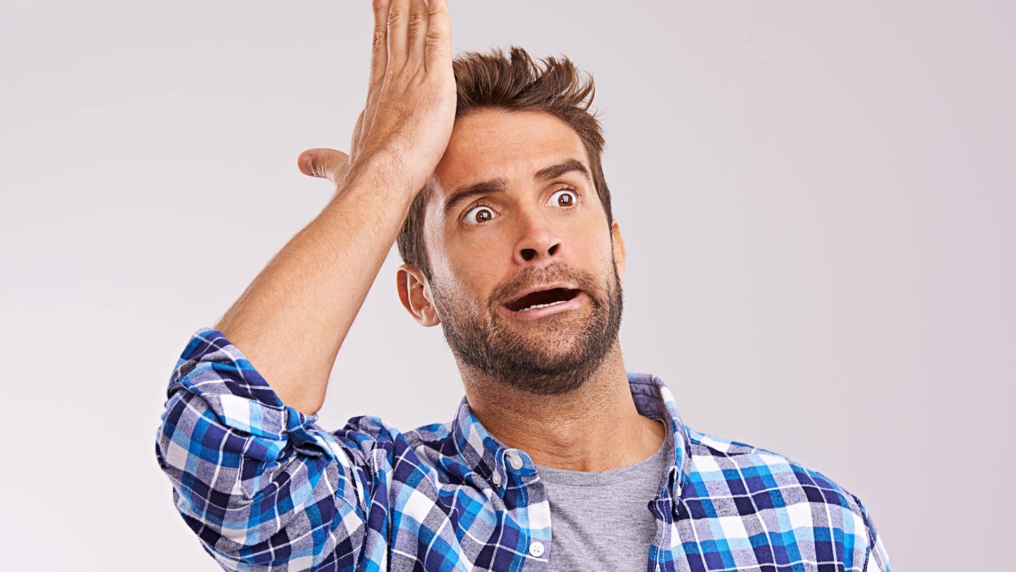 Duh. Studio shot of a young man looking forgetful against a gray background.