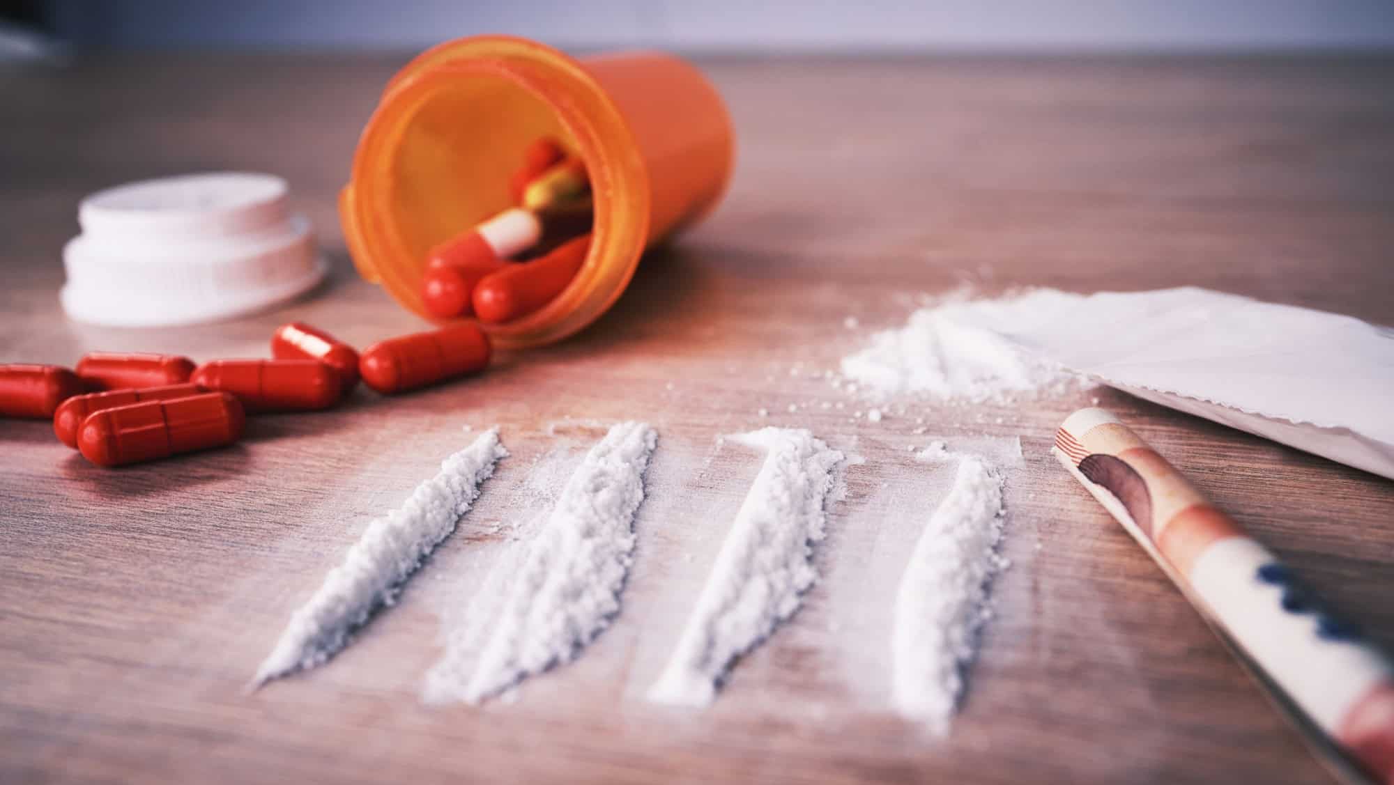 Drugs, addiction and cocaine on table with pills, social problem and crime in narcotics. White powder, mental health and rehabilitation to stop addictive substance abuse and trafficking illegal drug.