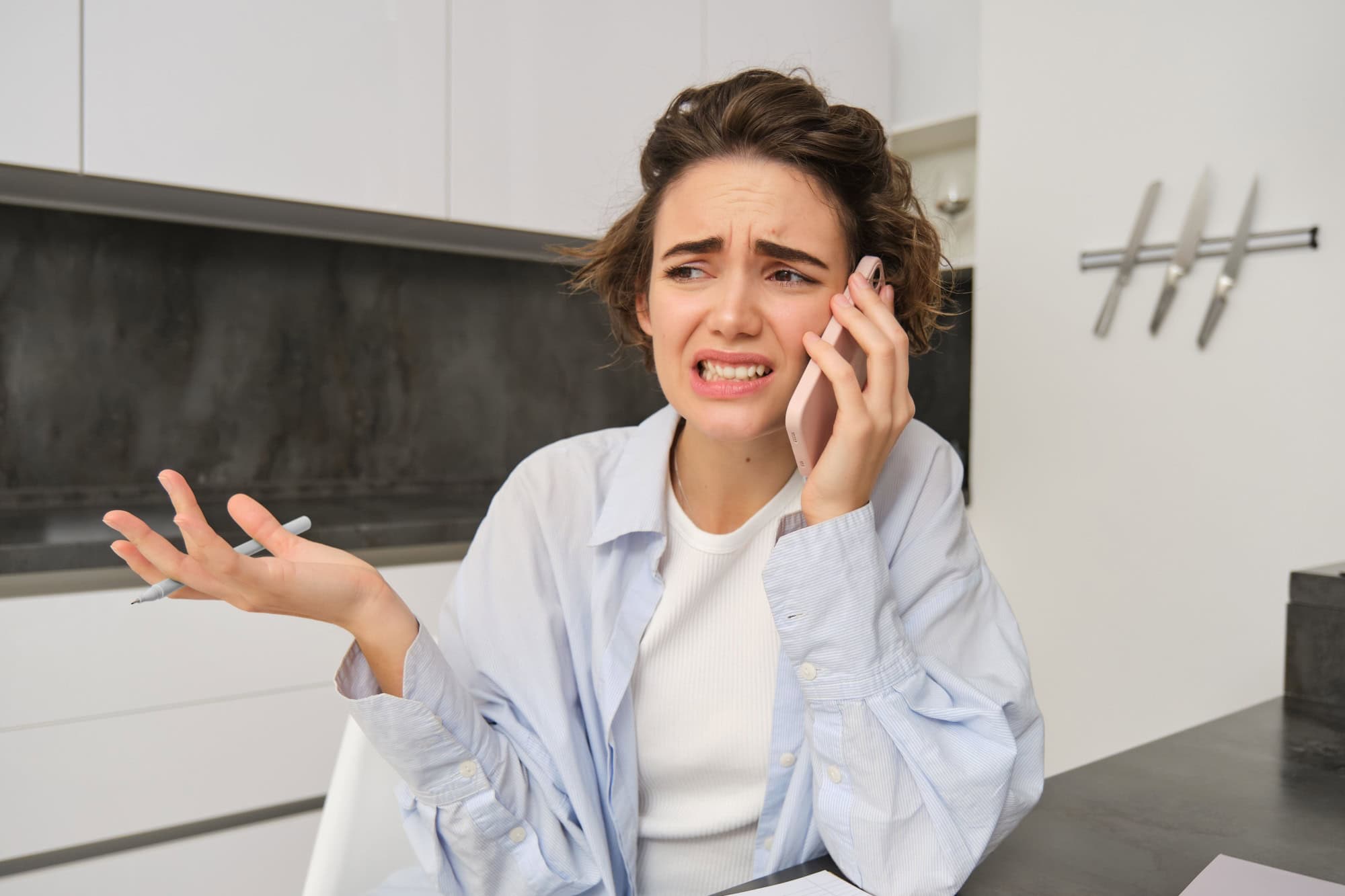 Portrait of woman with guilty face talking on mobile phone, sitting at home and having uncomfortable conversation over the telephone.