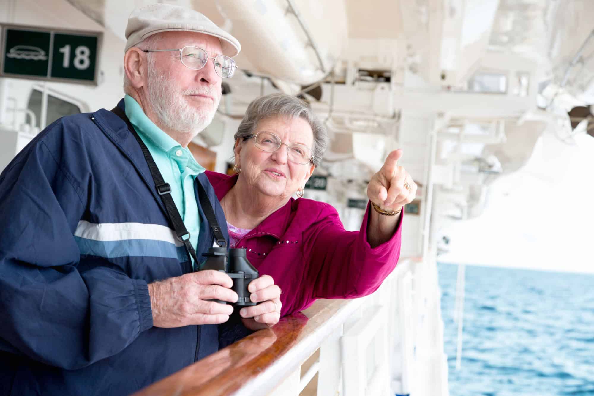 Senior Adult Couple Enjoying The View From Their Passenger Cruise Ship with Their Binoculars.