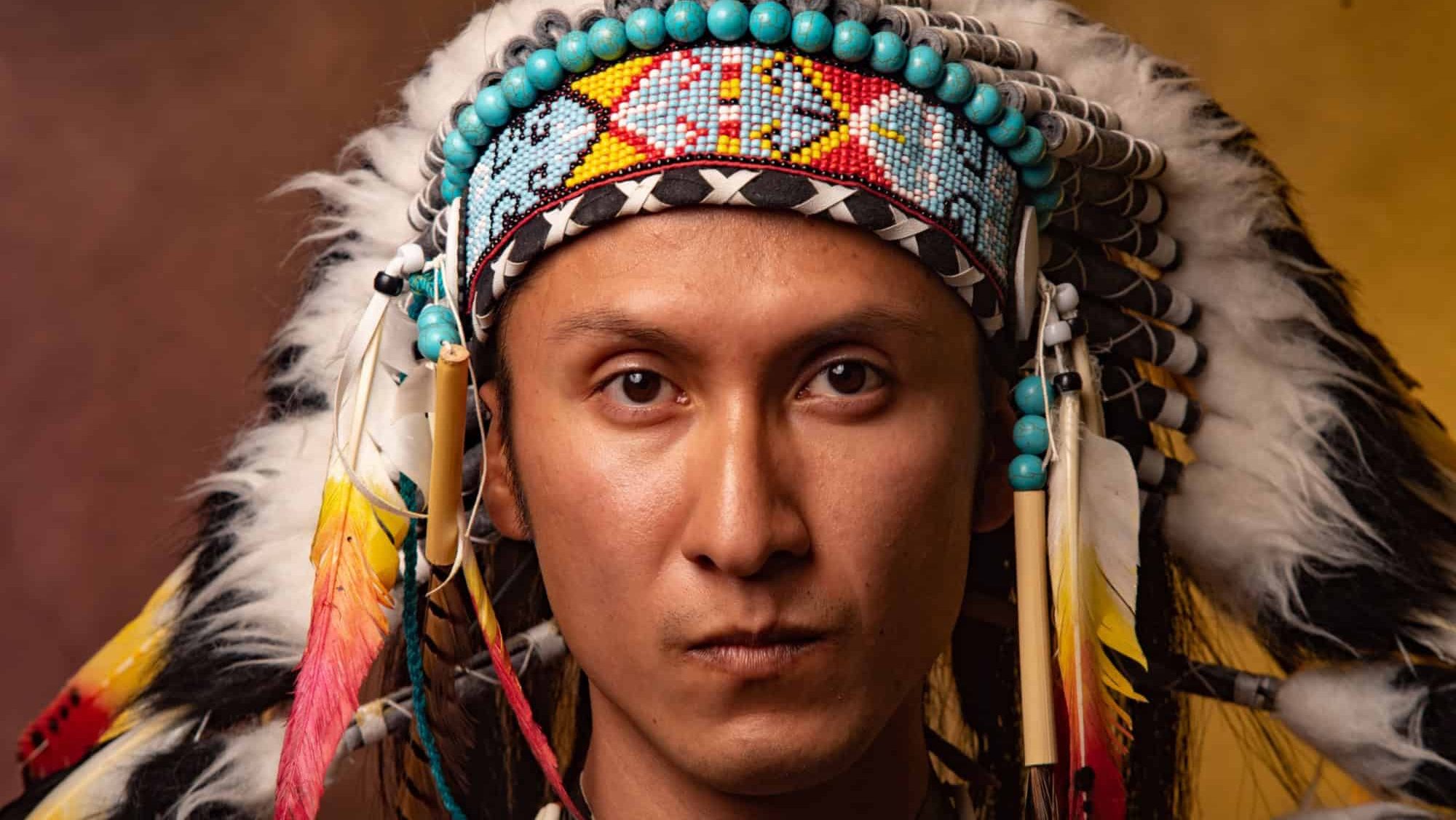 A man wearing a Native American headdress. The man is wearing a headdress with feathers and beads