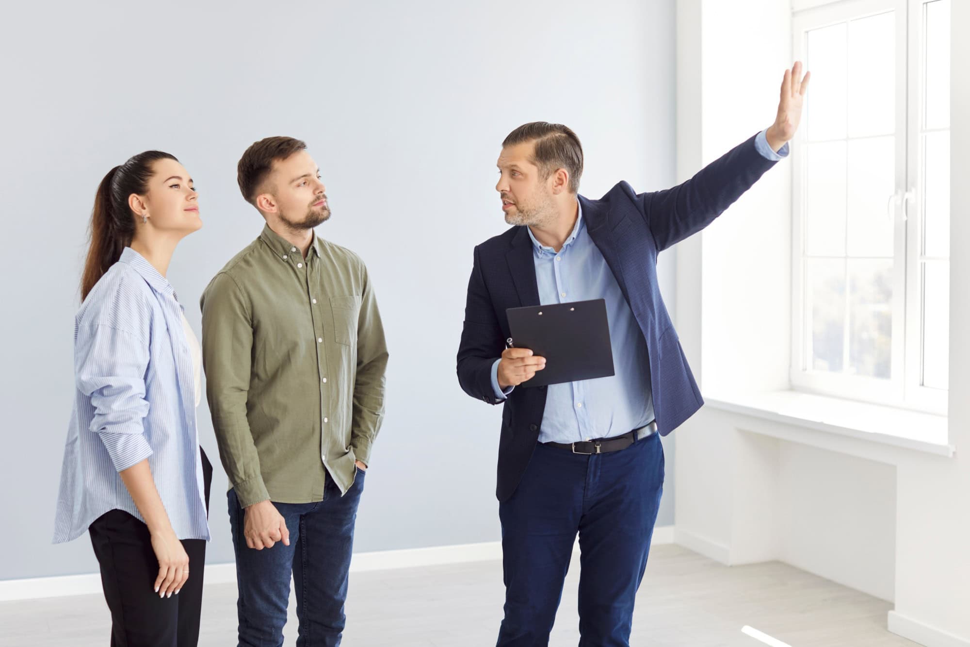 Real estate agent showing a house to a young couple, close-up. Family in an empty apartment listening to a businessman. Concept new house, estate broker, mortgage agreement, investment
