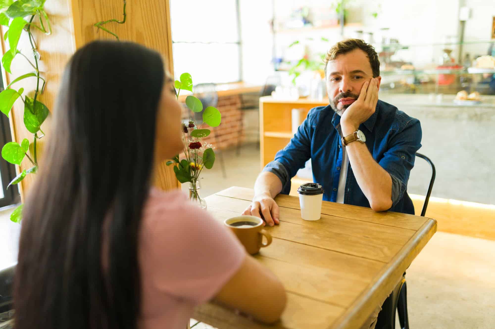 Bored man ignoring his girlfriend while sipping coffee at the cafe, highlighting communication issues in their troubled relationship