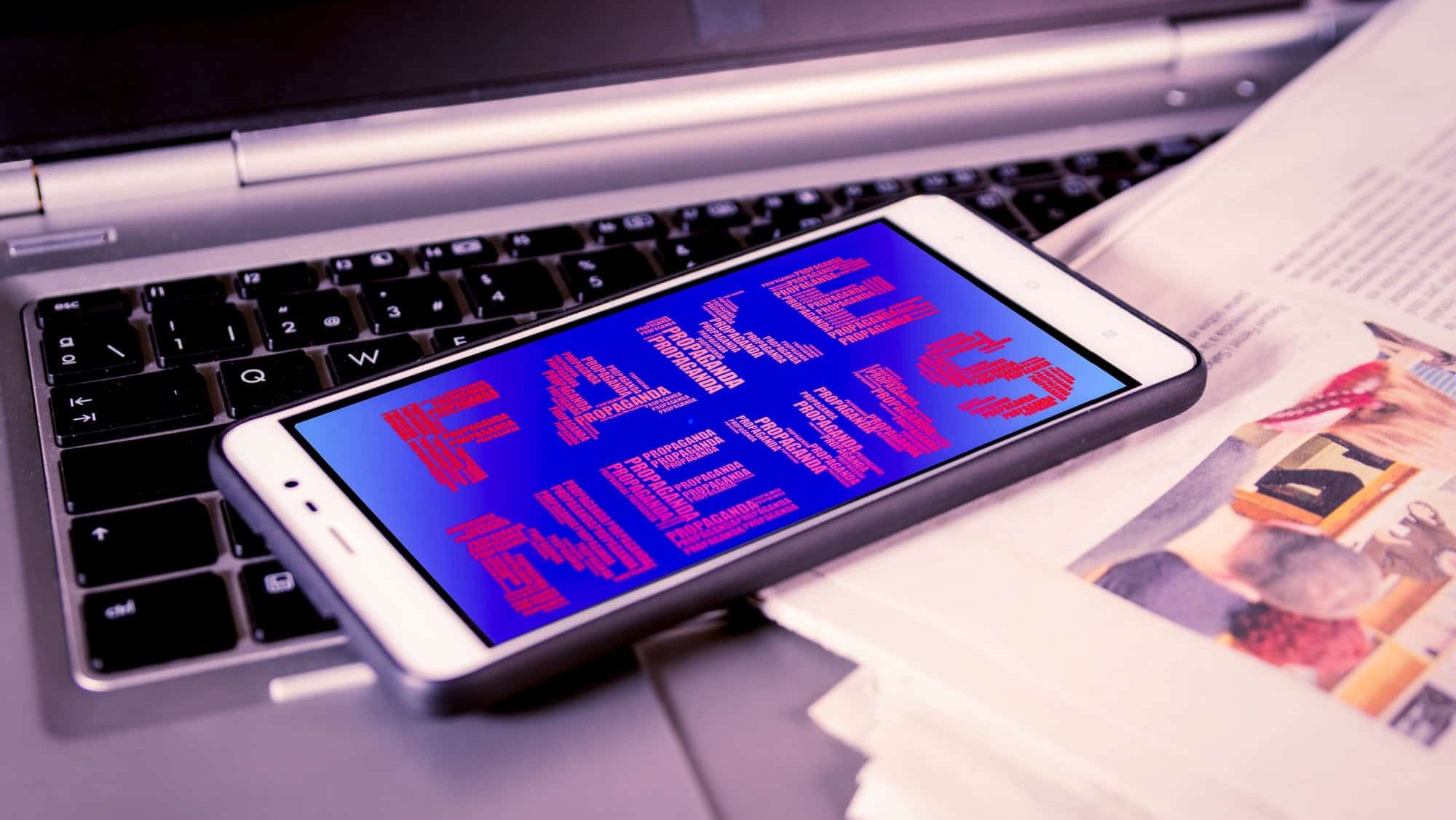 Smartphone with red Fake News words on screen over a newspaper. HOAX and Fake news concept.