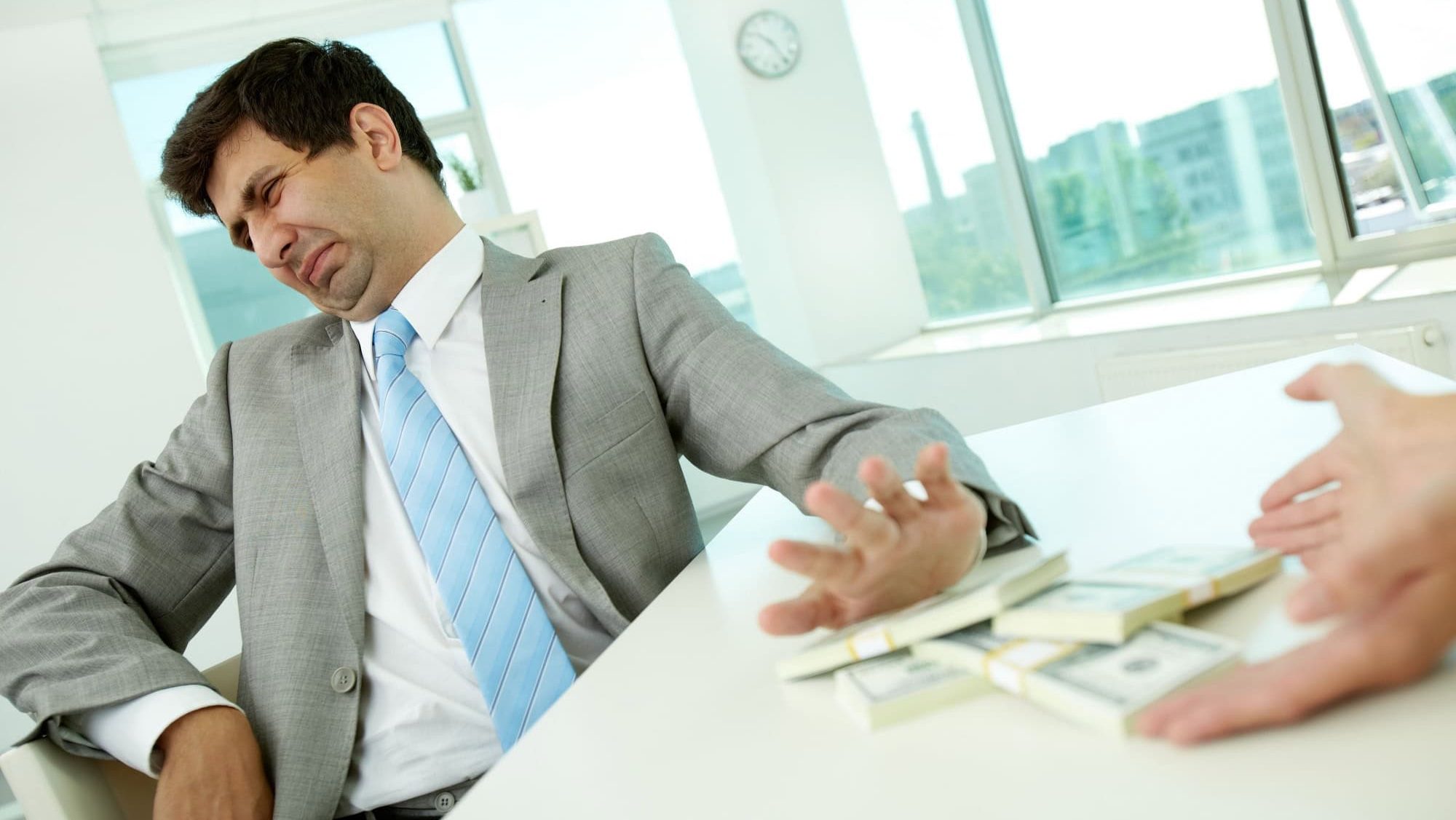 Image of disgusted male employee moving dollar bills away and refusing to take bribe
