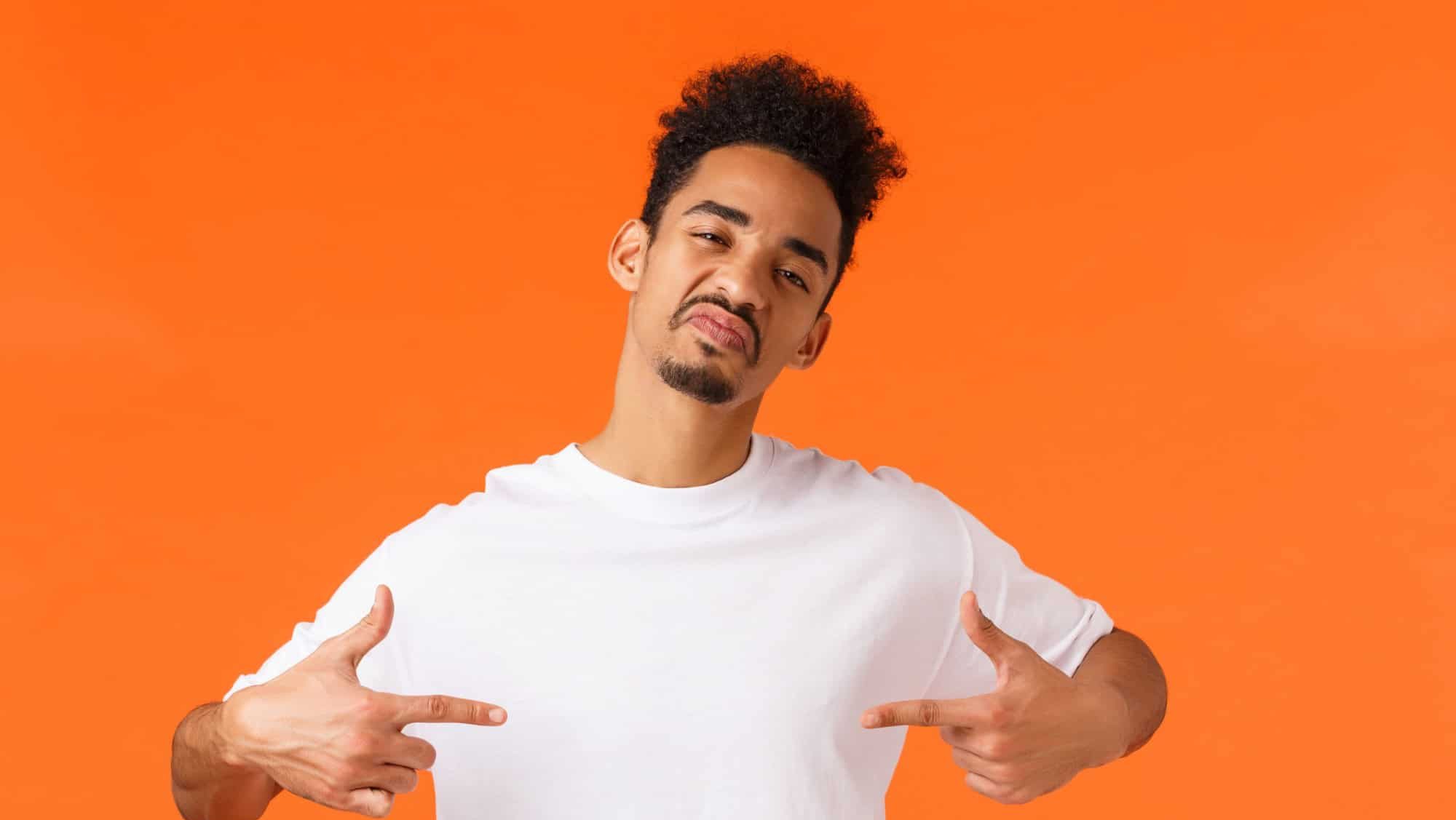 Sassy and confident assertive african-american man, acting cool and cheeky, pointing himself proud, boastful standing orange background, show-off, making impression, wearing white t-shirt