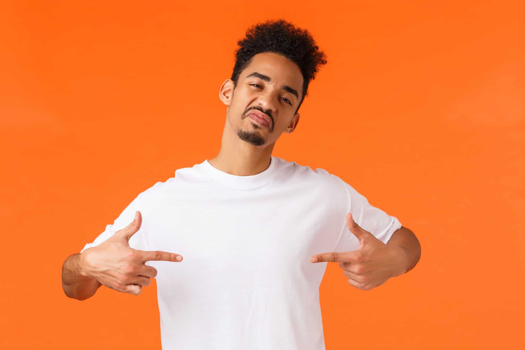 Sassy and confident assertive african-american man, acting cool and cheeky, pointing himself proud, boastful standing orange background, show-off, making impression, wearing white t-shirt