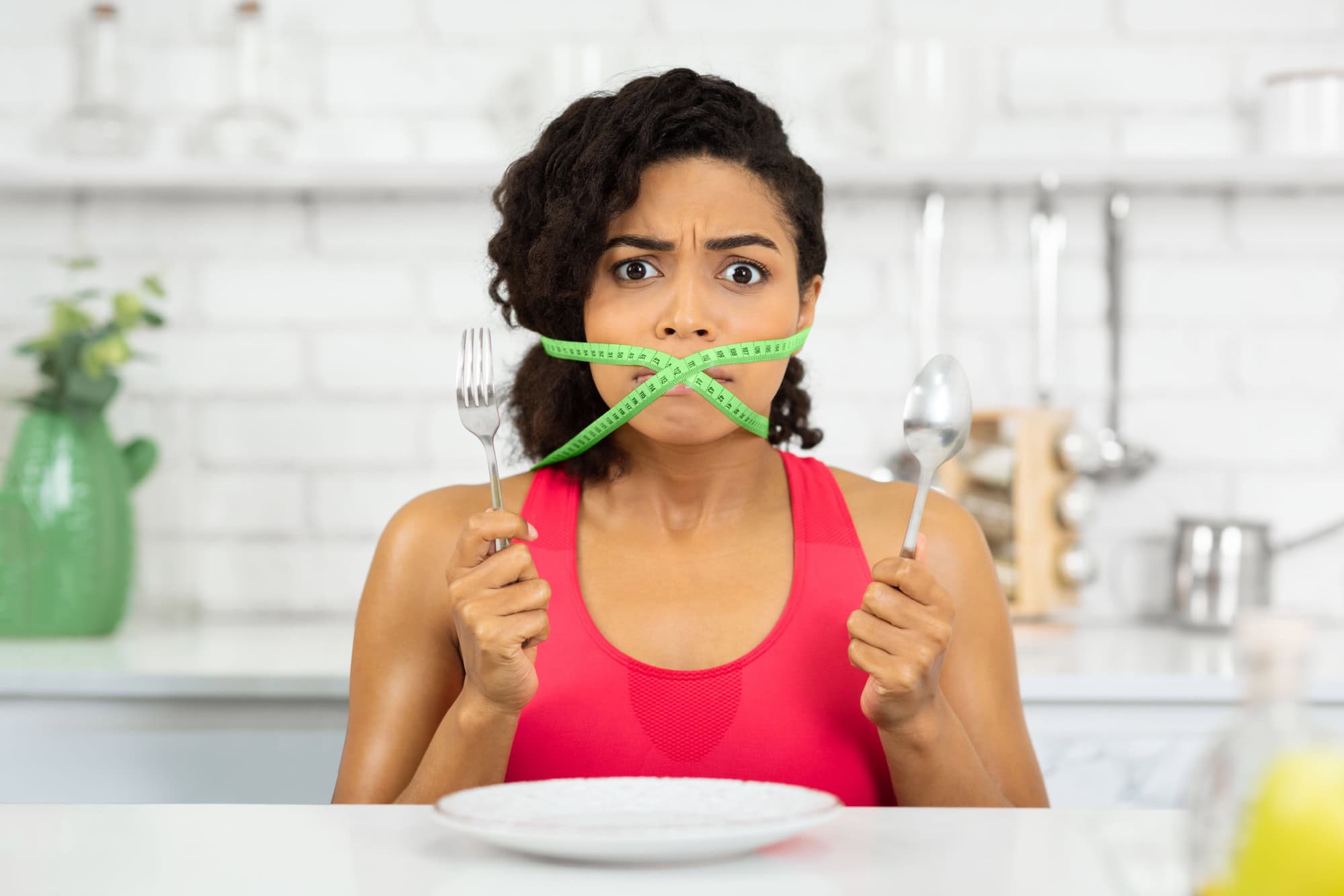 Diet Restriction Concept. Portrait of young frustrated black girl with a green measuring tape around her mouth