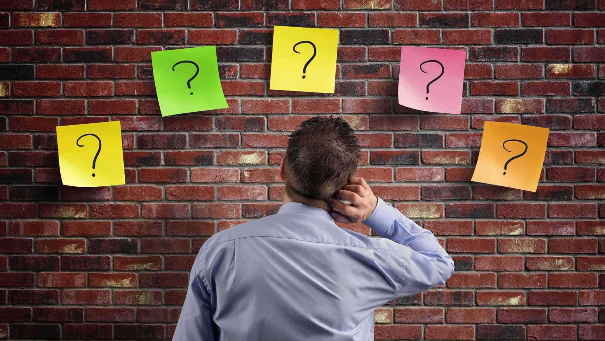 Choice and decisions: businessman thinking with question marks written on adhesive notes stuck to a brick wall