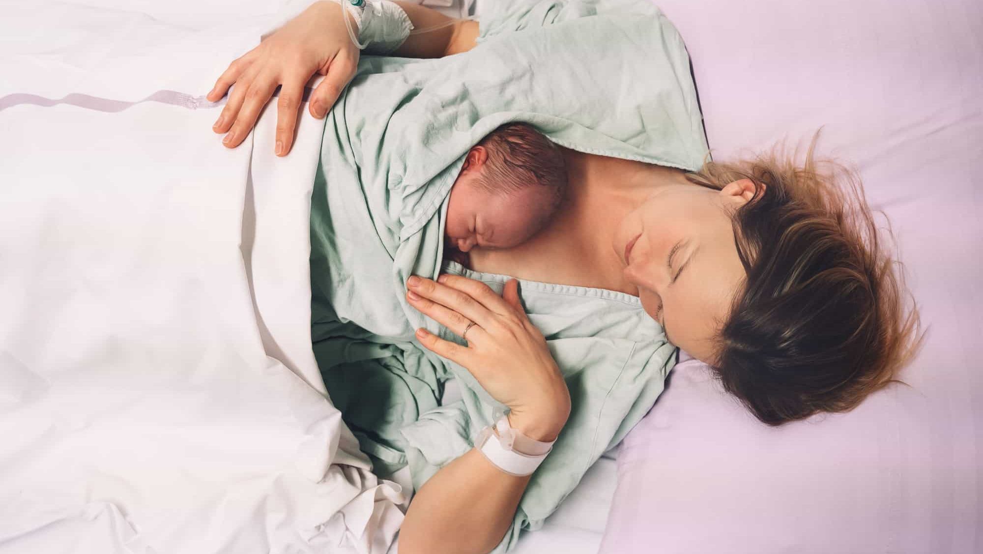 Mother and newborn. Child birth in maternity hospital. Young mom hugging her newborn baby after delivery. Woman giving birth. First moments of baby life after labor.