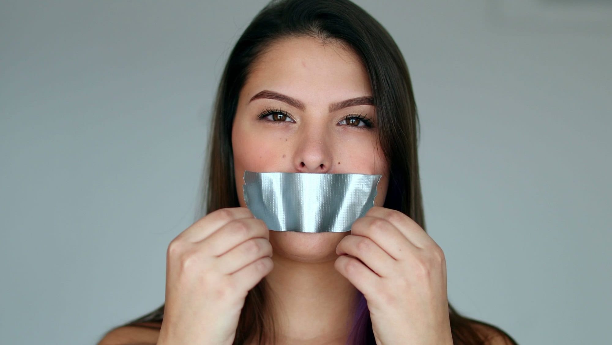 Assertive woman removing tape from mouth feeling relief and freedom to speak