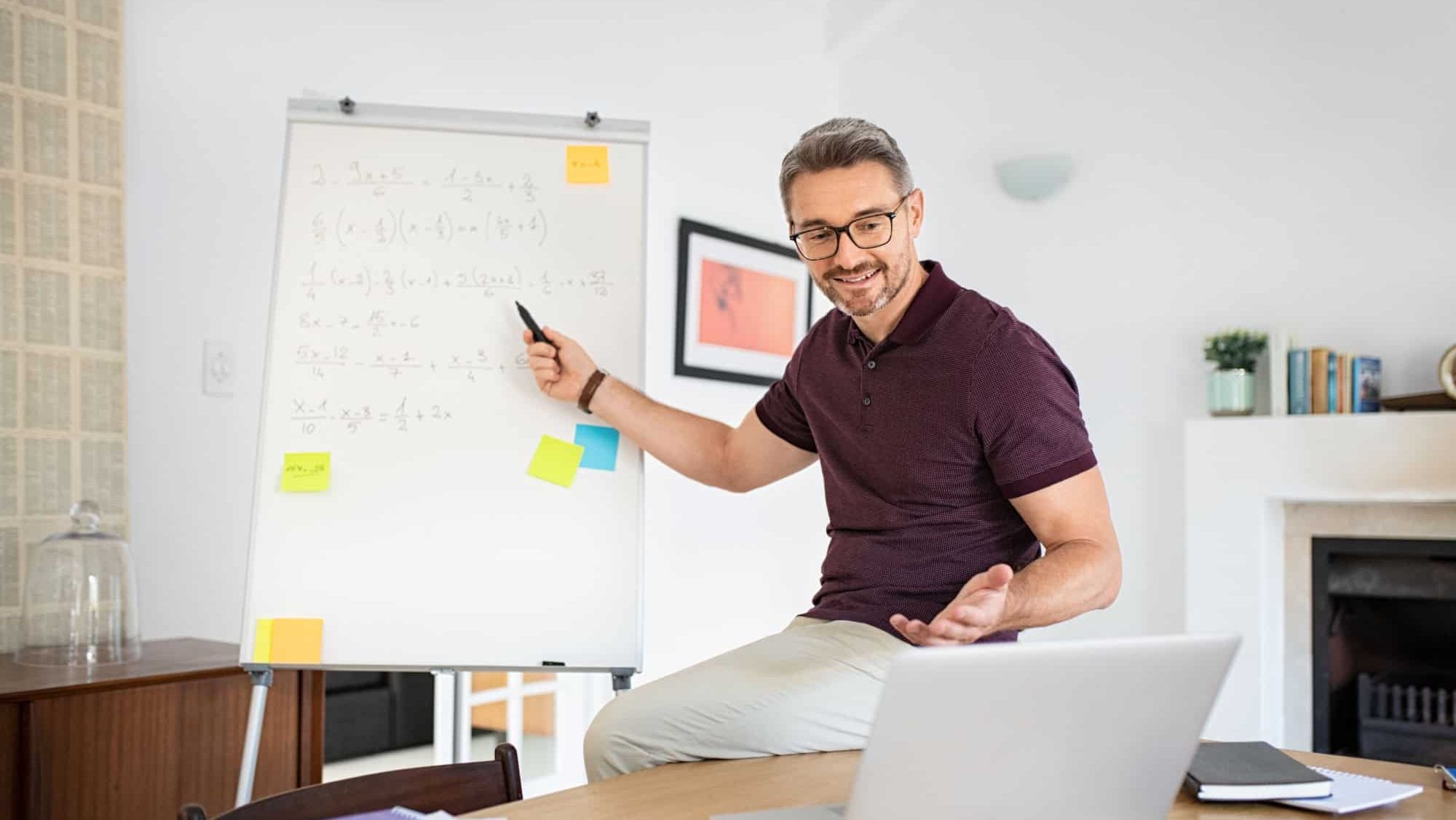 Mature teacher having online class through video call and explaining maths. Teacher teaching students maths on video call at home: e-learning via interactive platform. Mature math professor teaching.