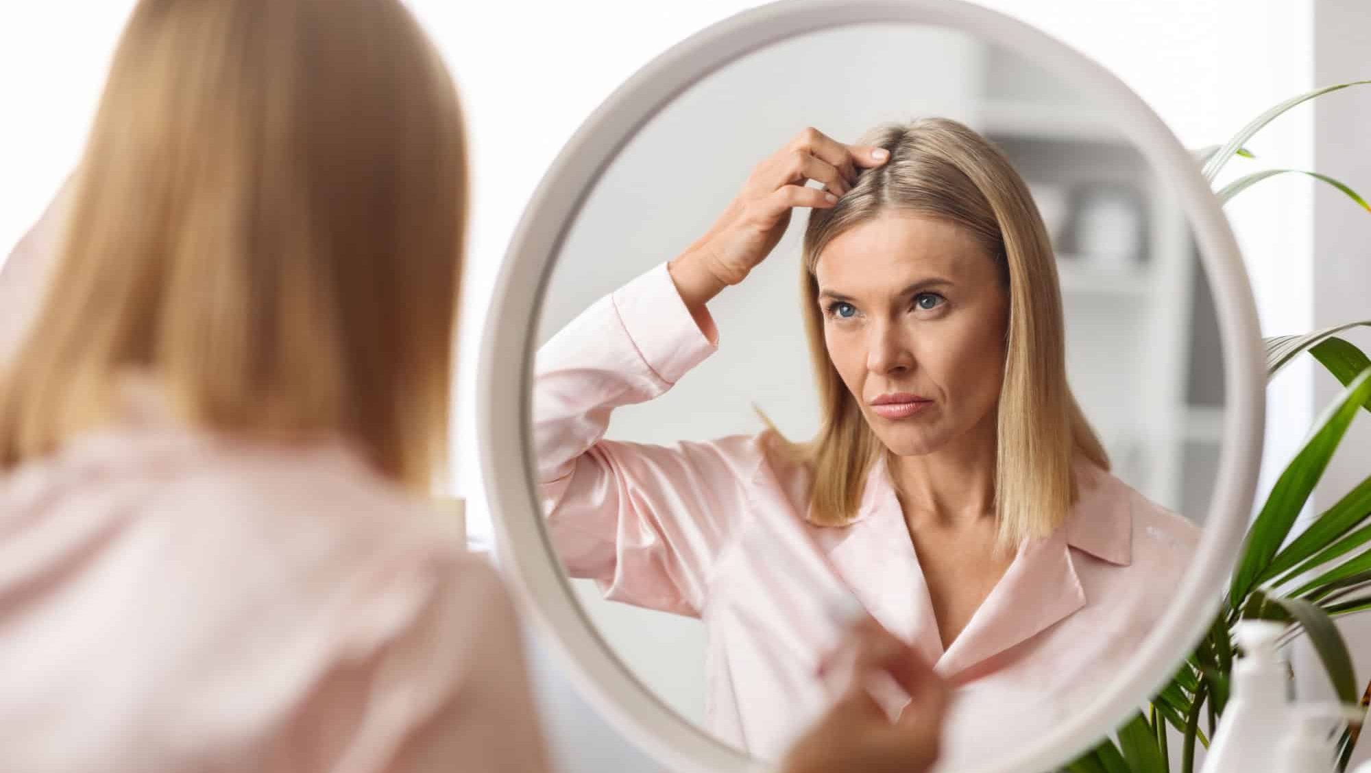 Upset Middle Aged Lady Looking In Mirror At Her Hair Roots While Making Beauty Routine At Home, Frustrated Mature Woman Suffering Dandruff Or Hairloss Problem
