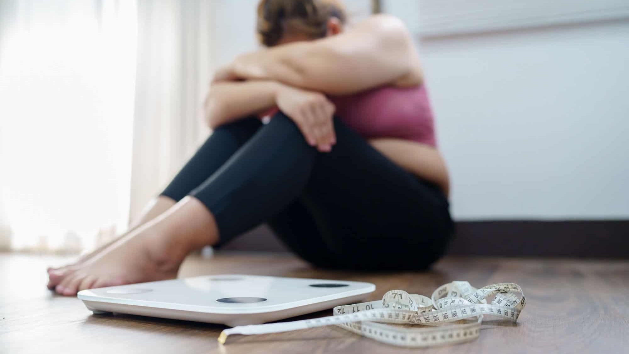 Obese Woman with fat upset bored of dieting Weight loss fail Fat diet and scale sad asian woman on weight scale at home weight control.