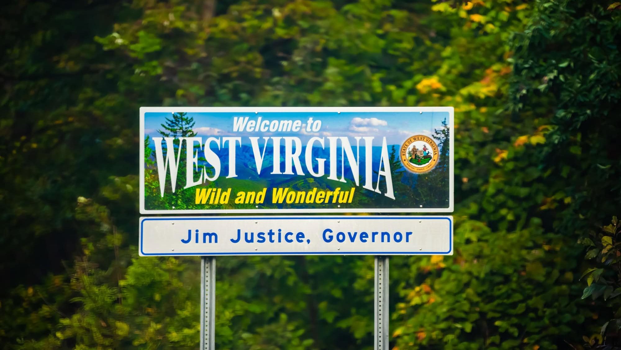 Welcome to West Virginia sign text Wild and Wonderful with mountains picture and blue sky by Virginia border and Jim Justice Governor