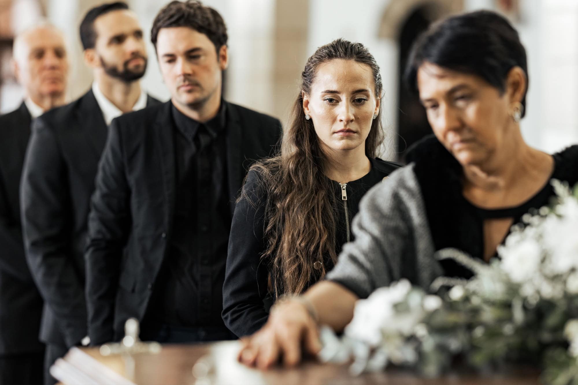 Funeral, goodbye and family with a coffin in a church during a service in death, mourning and grief. Respect, greeting and sad people in a row with a casket in a cathedral for a burial or memorial