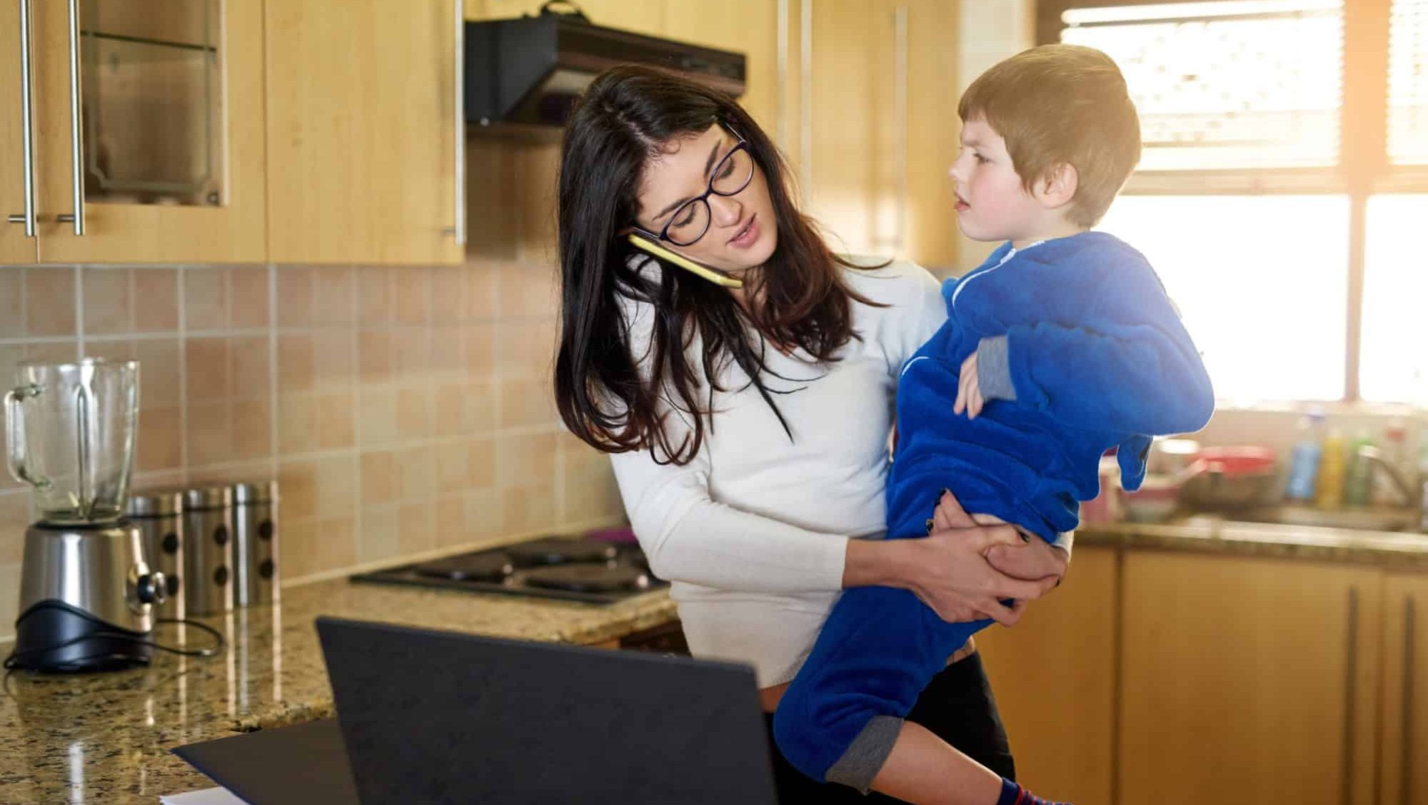 Mother, child and phone call for remote work with stress in home, challenge and talking to contact on laptop in kitchen. Mom, kid and freelancer multitask on mobile, parenting and family together