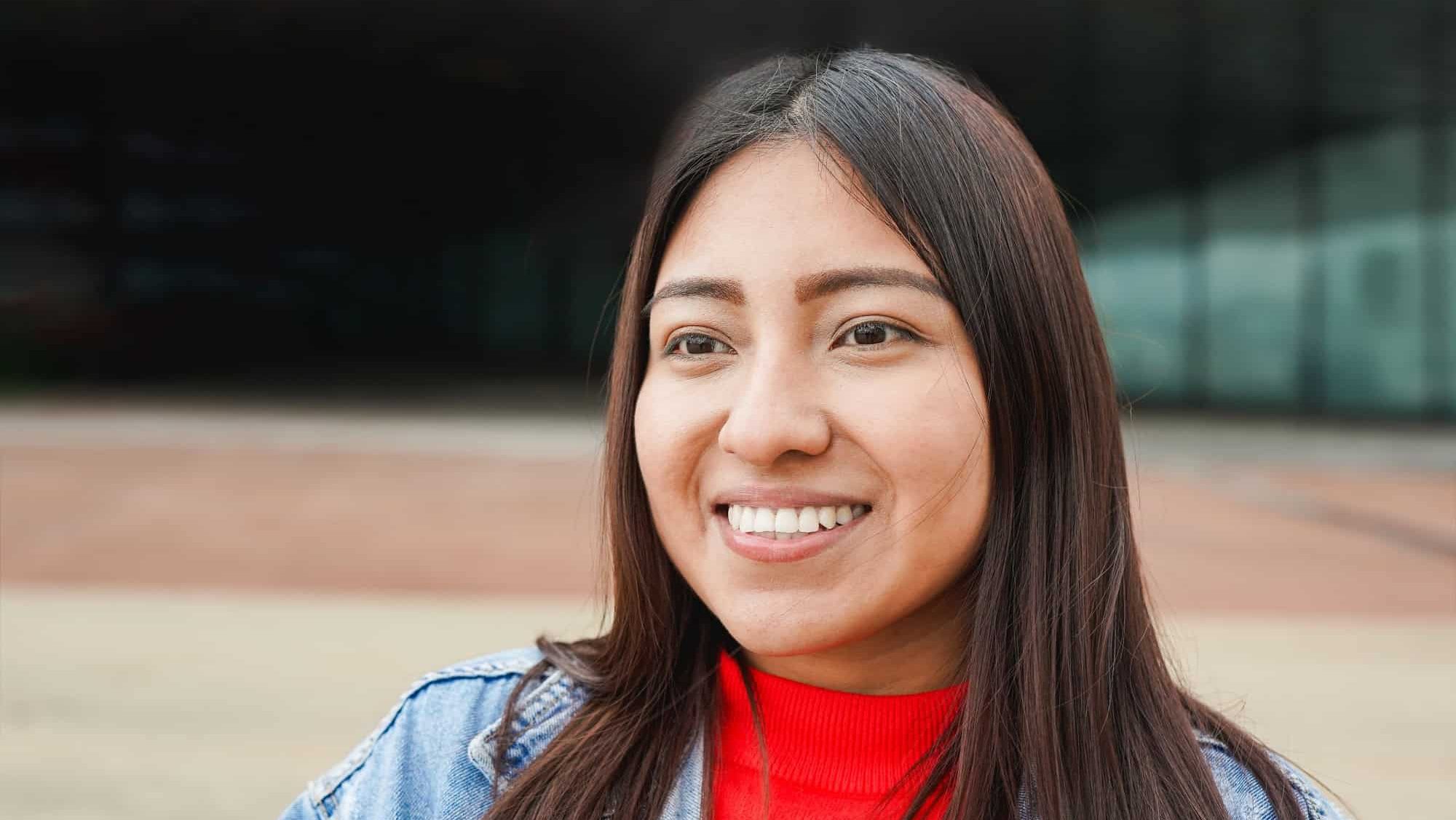 Portrait of native american woman smiling in front of camera with city in background - Indigenous girl outdoor