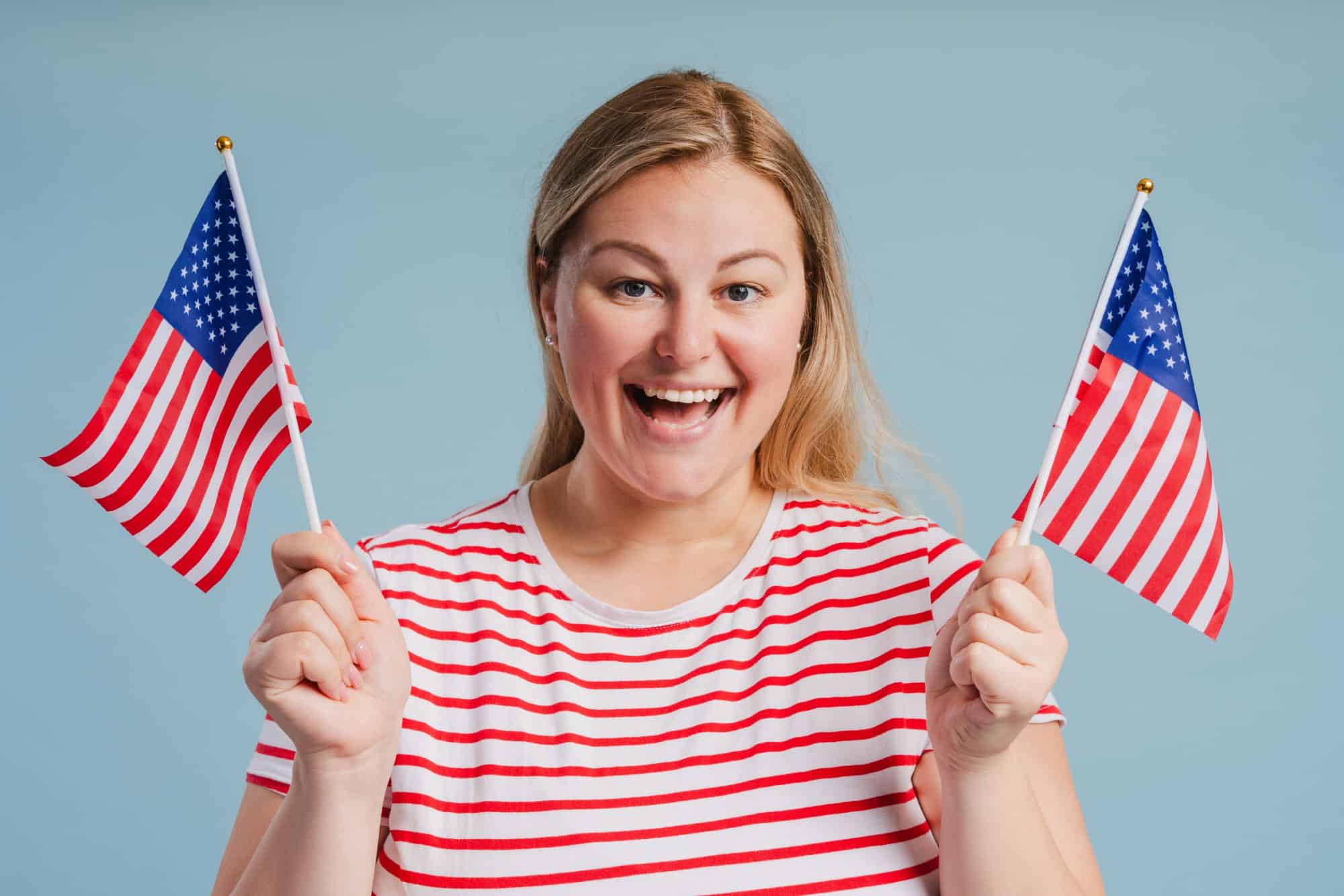 Portrait of happy young plus size woman posing with two American flags isolated on blue background in studio