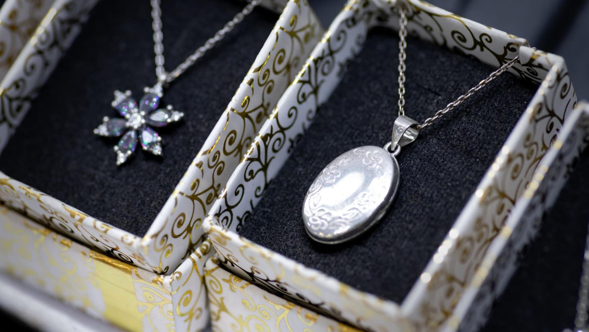 A beautifully crafted silver oval locket pendant necklace with engraved patterns, displayed in an elegant jewelry box