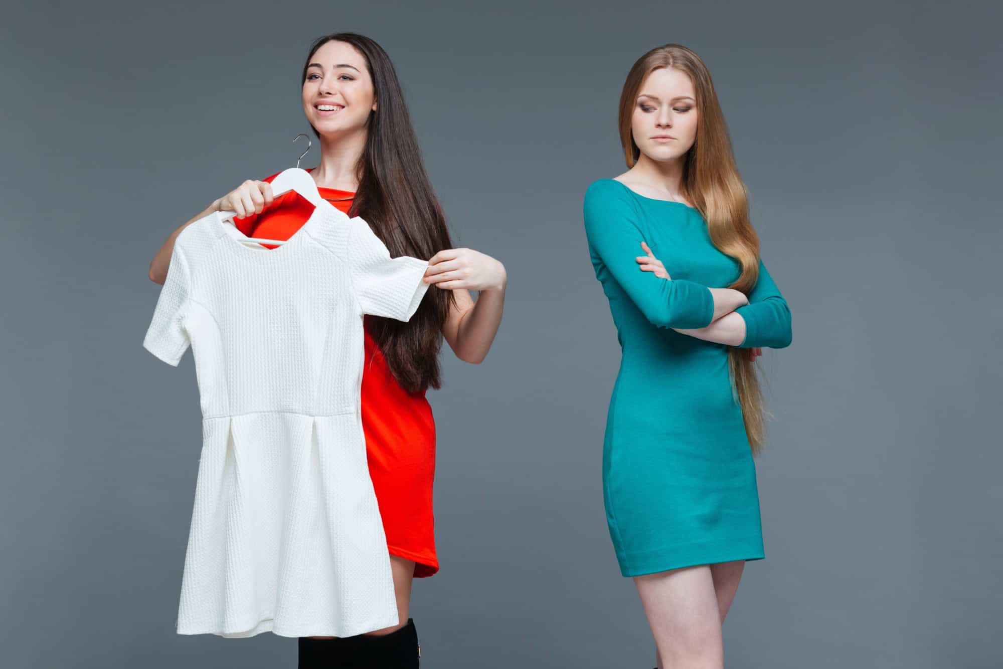 Happy cheerful young woman and envious angry female on shopping over grey background