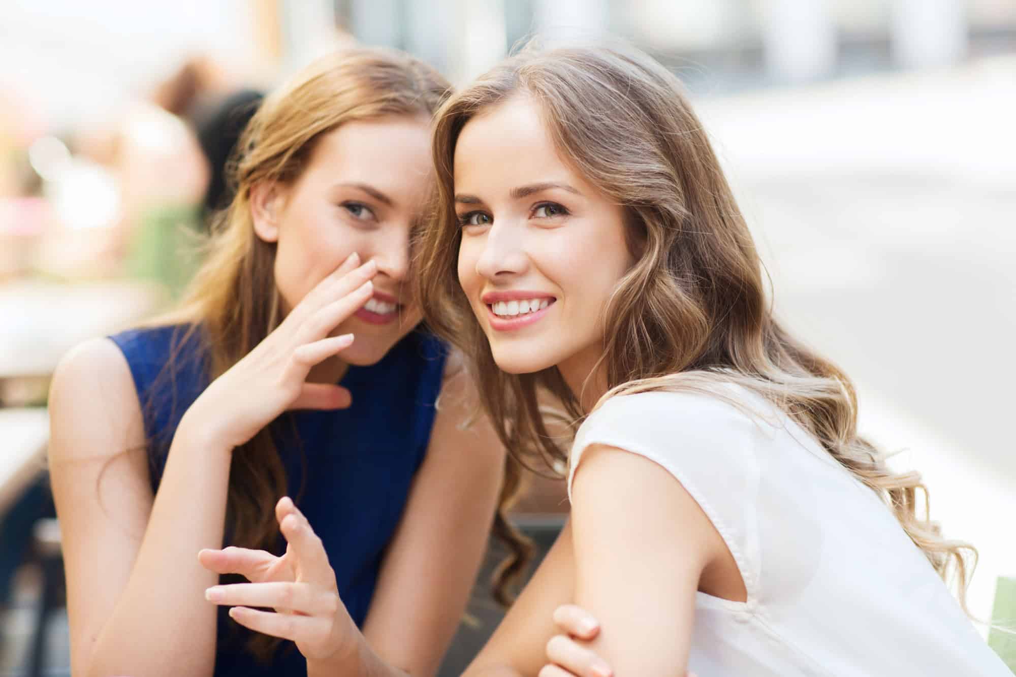 People communication and friendship concept - smiling young women drinking coffee or tea and gossiping at outdoor cafe
