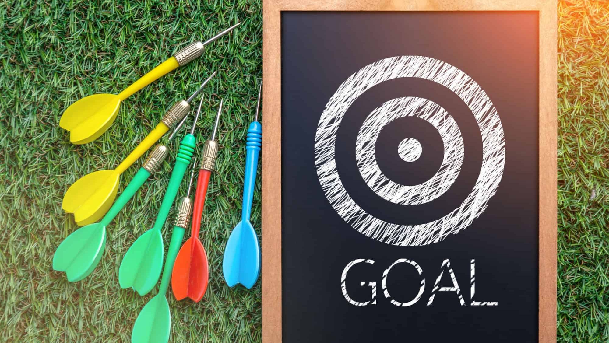 business vision concept with goal dart hand drawn on chalkboard with colorful dart arrow on grass floor.jpg