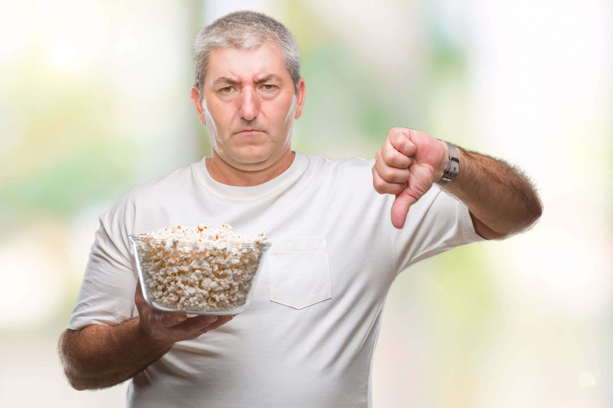 Handsome senior man eating popcorn over isolated background with angry face, negative sign showing dislike with thumbs down, rejection concept