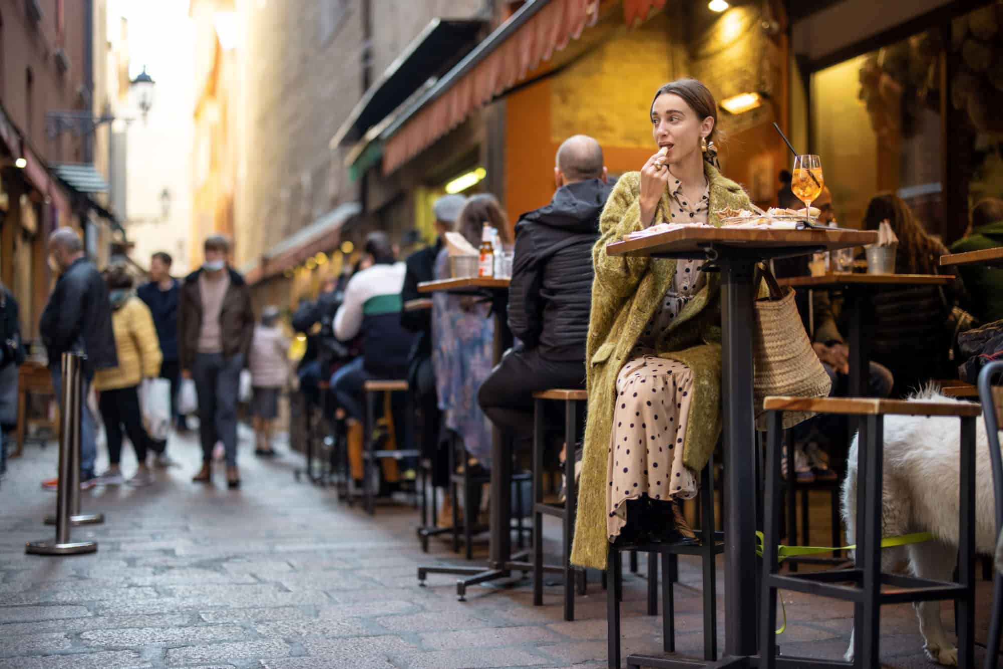 Woman sitting on crowded street at bar or restaurant outdoors in Bologna city. Concept of Italian lifestyle and gastronomy