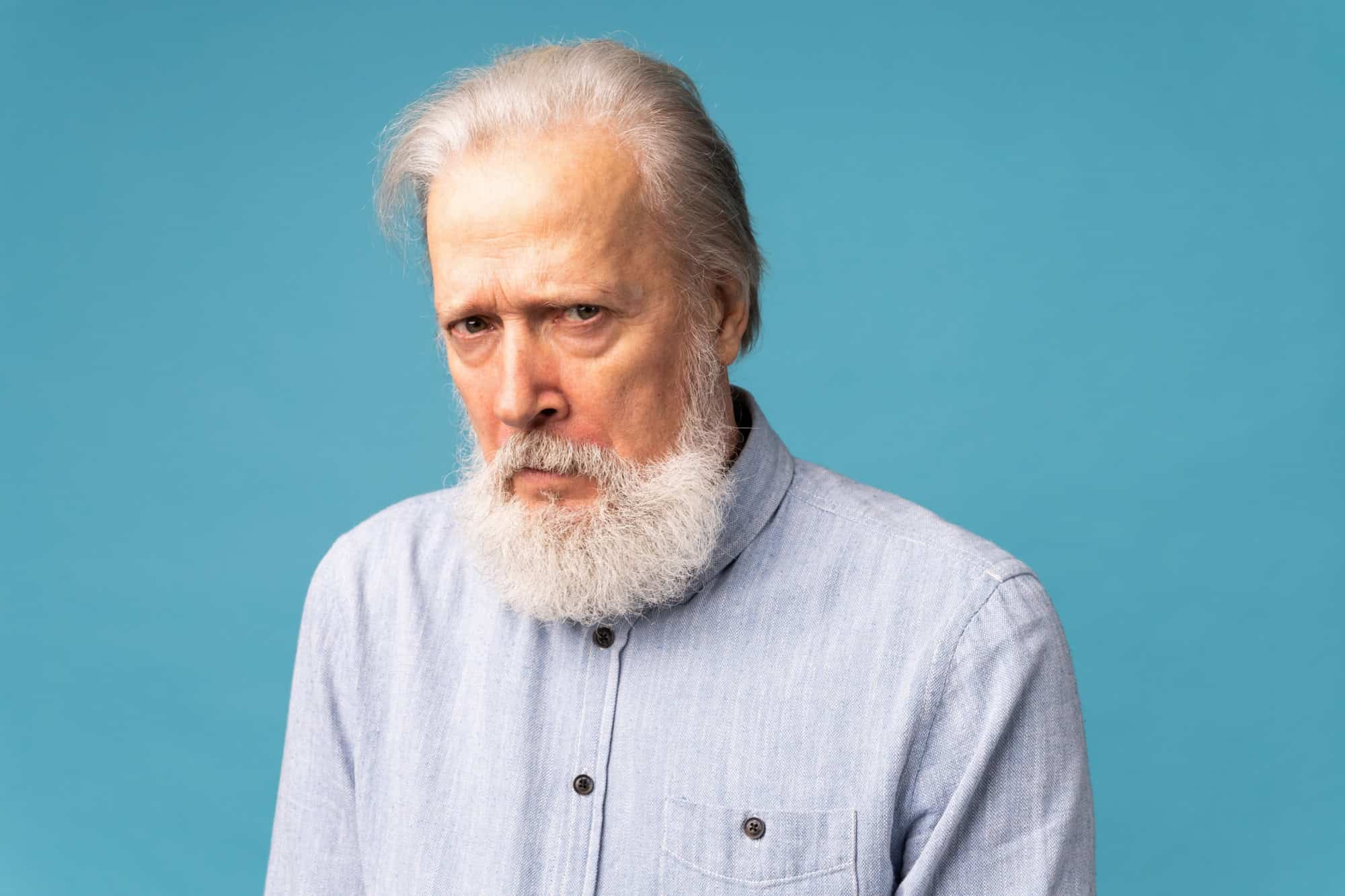 Portrait of unhappy grumpy pissed off senior mature man on blue background. Negative human emotions, face expression feelings